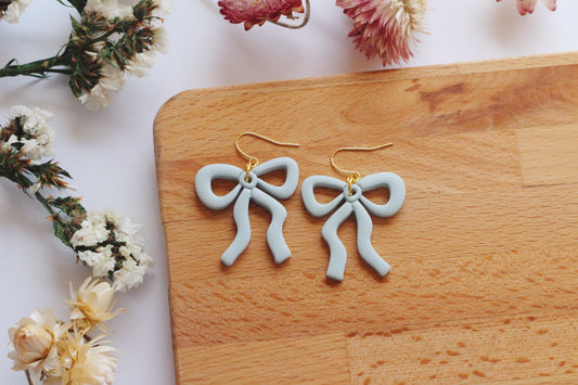 Bow-shaped earrings on a wooden board with flowers in the background