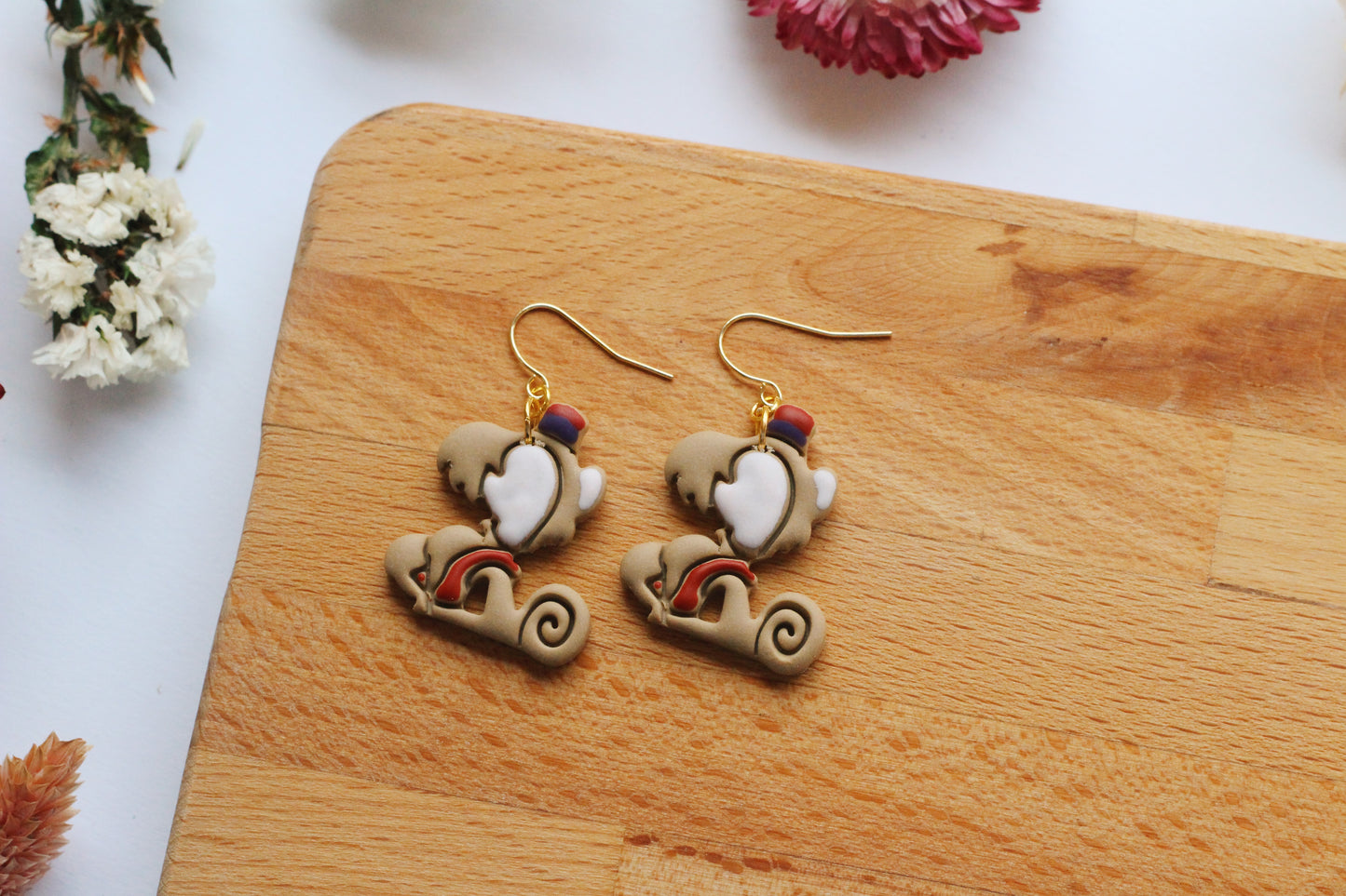 Monkey earrings with rainbow designs on a wooden board.