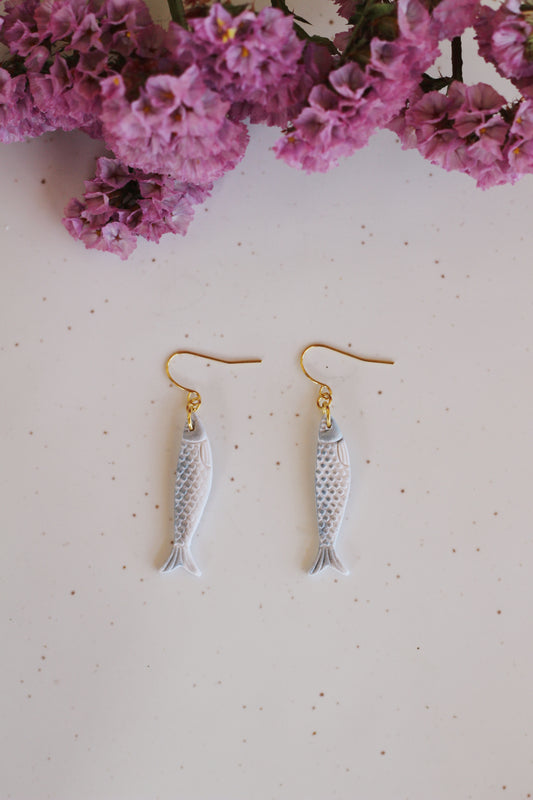 Sardine-shaped earrings on a light pink background with purple flowers.