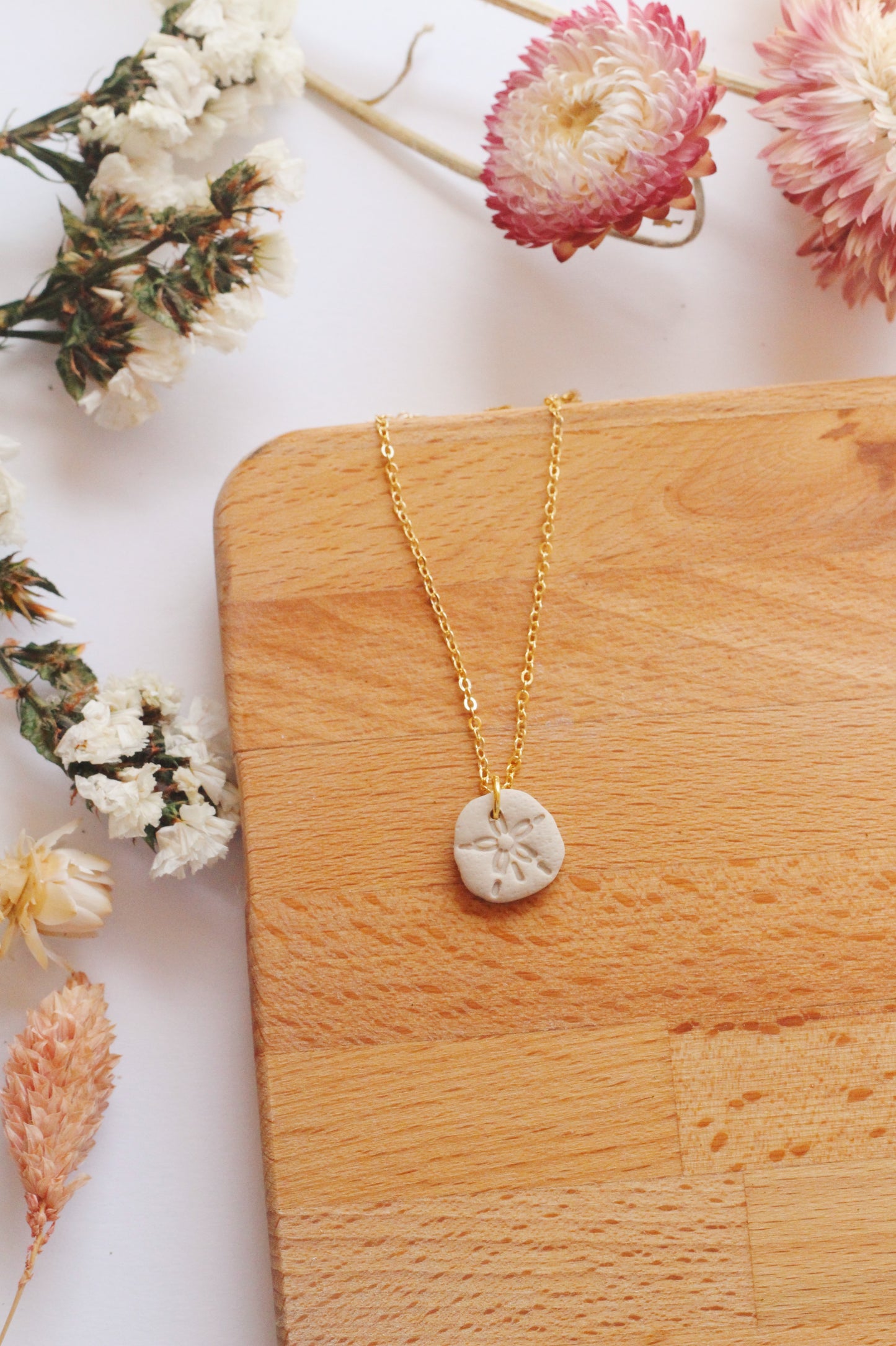 Gold necklace with a sand dollar pendant on a wooden surface with flowers