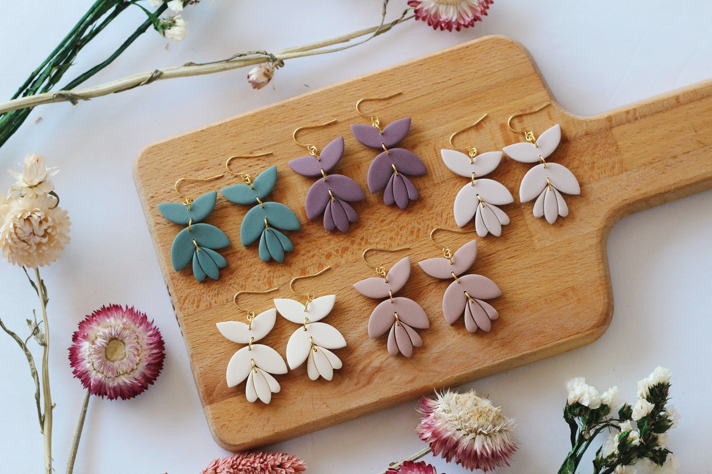 Set of colorful earrings on a wooden board with flowers around