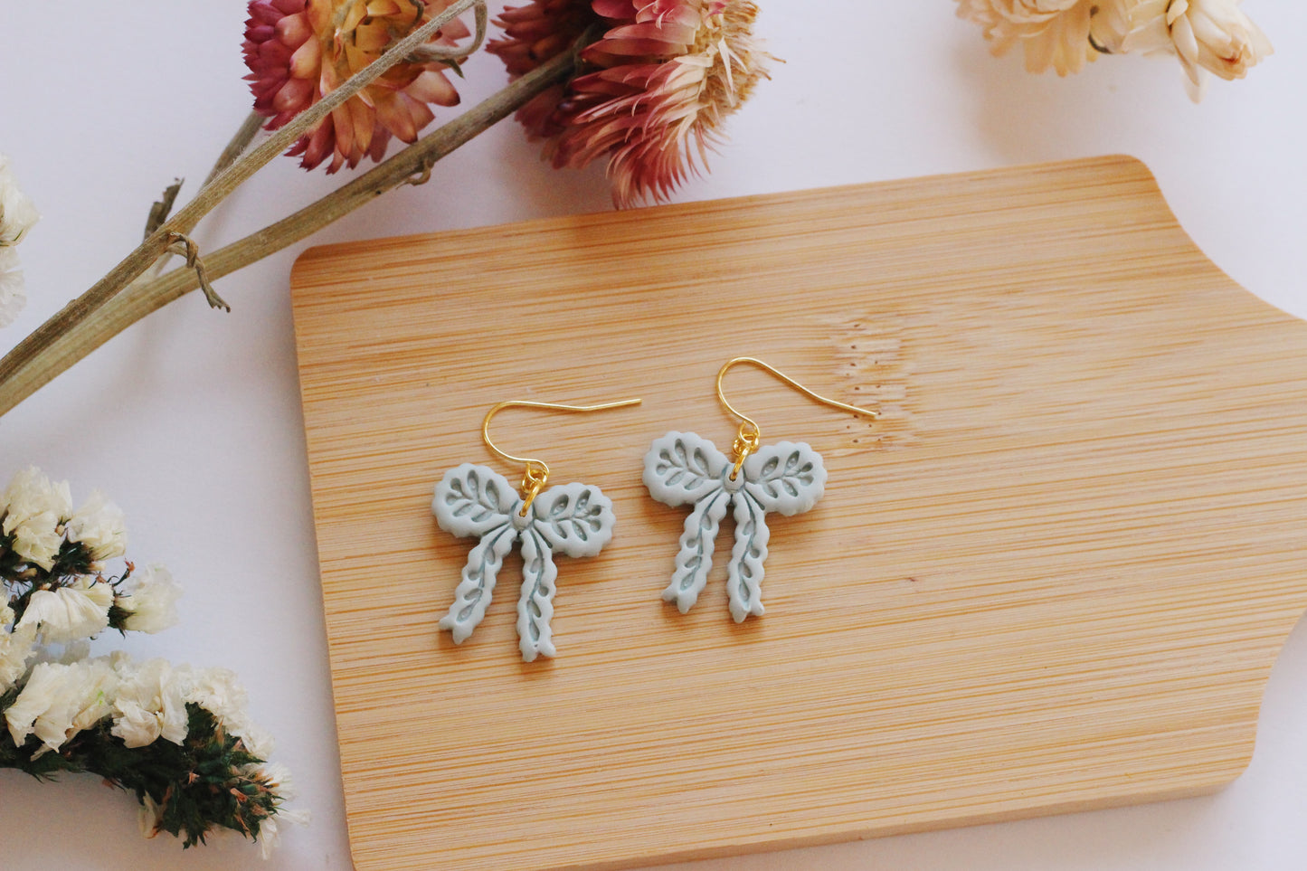 Bow-shaped earrings on a wooden board with flowers in the background