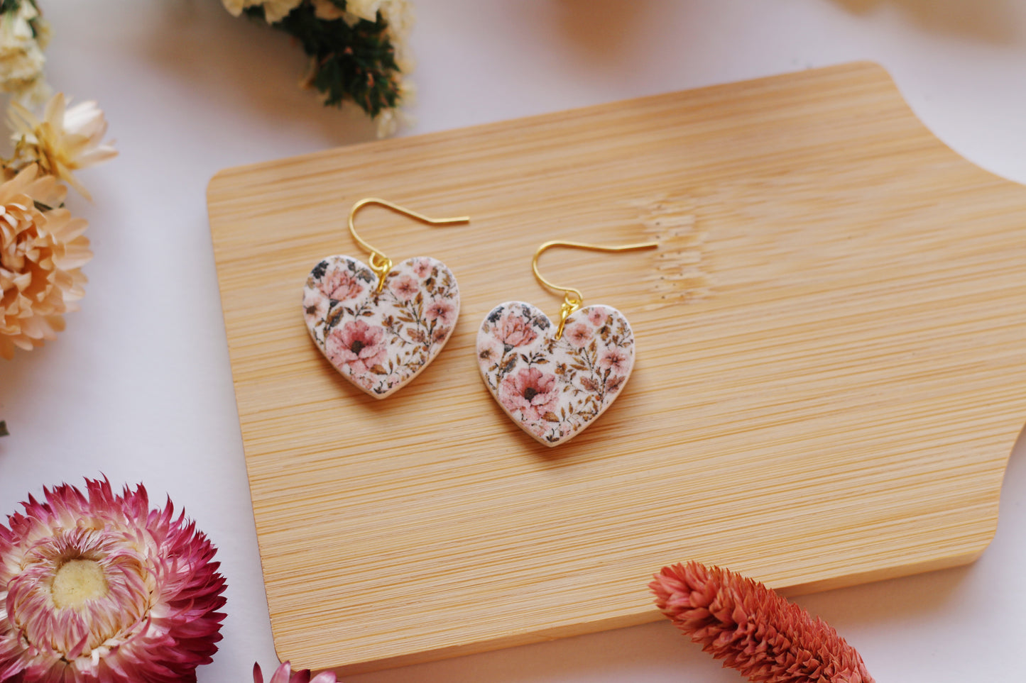 Heart-shaped floral earrings on a wooden board with flowers around