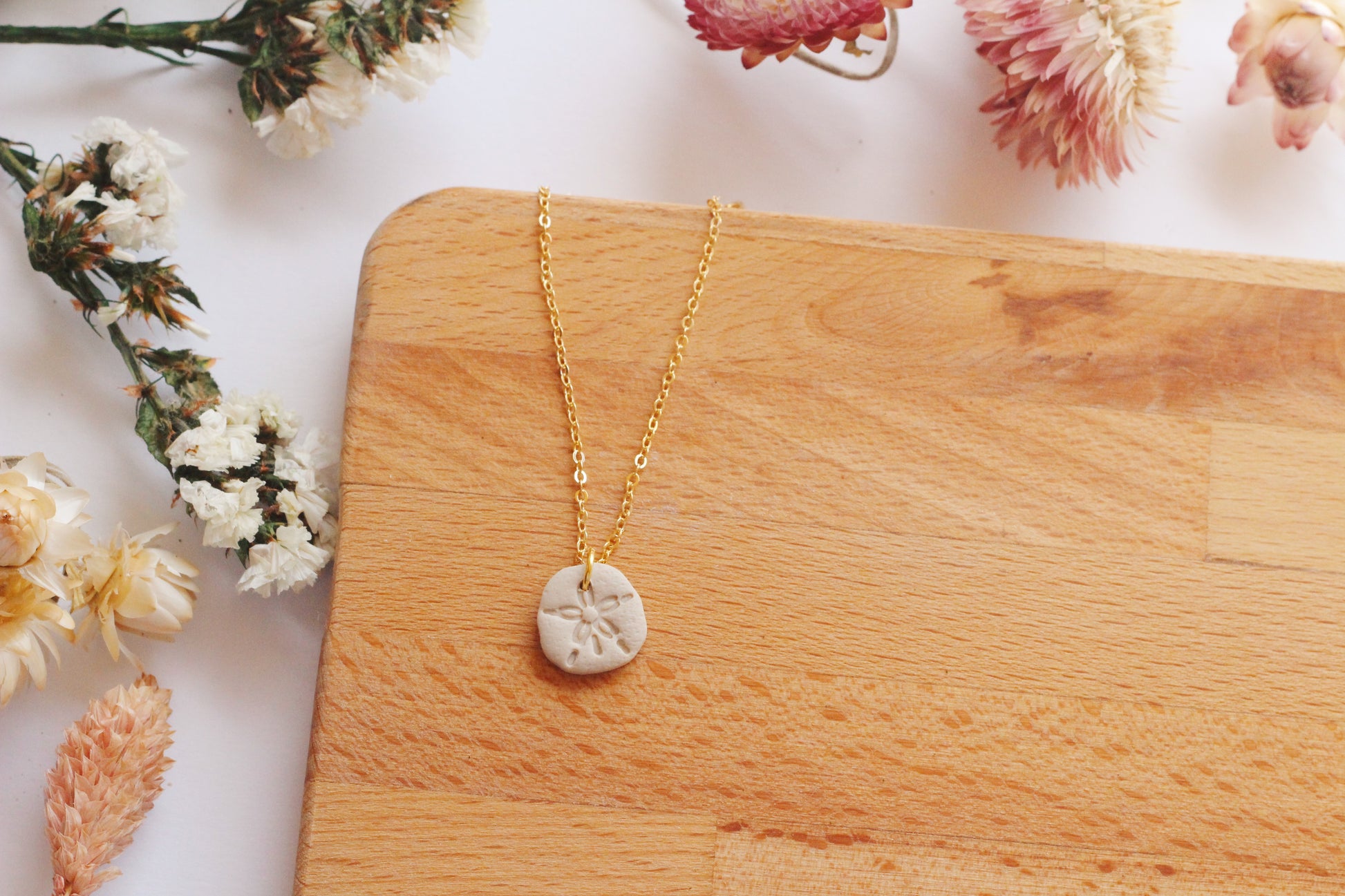 Gold necklace with a sand dollar pendant on a wooden board surrounded by flowers