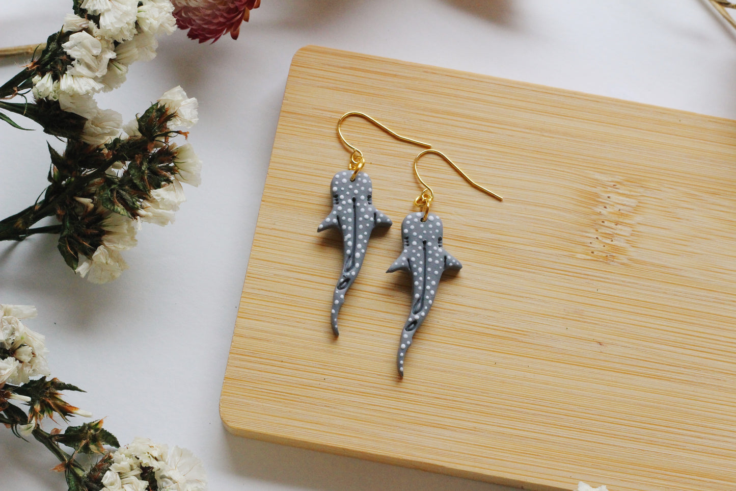 Shark-shaped earrings on a wooden board with flowers in the background