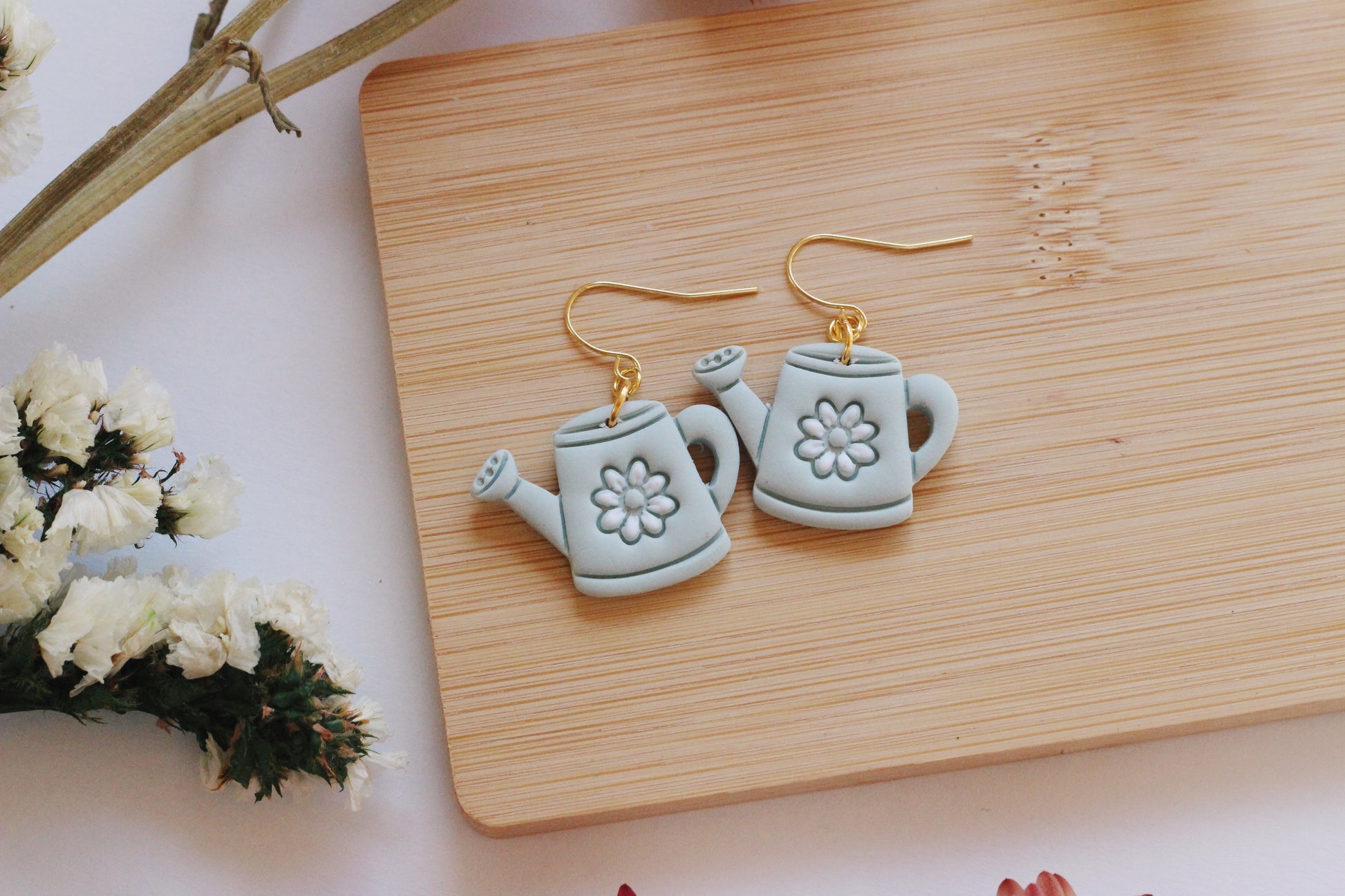 Tea pot-shaped earrings on a wooden board with flowers in the background