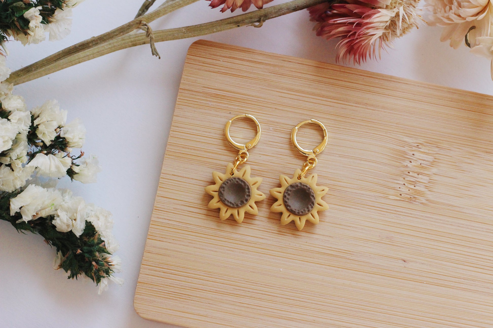 Sunflower-shaped earrings on a wooden board with flowers in the background