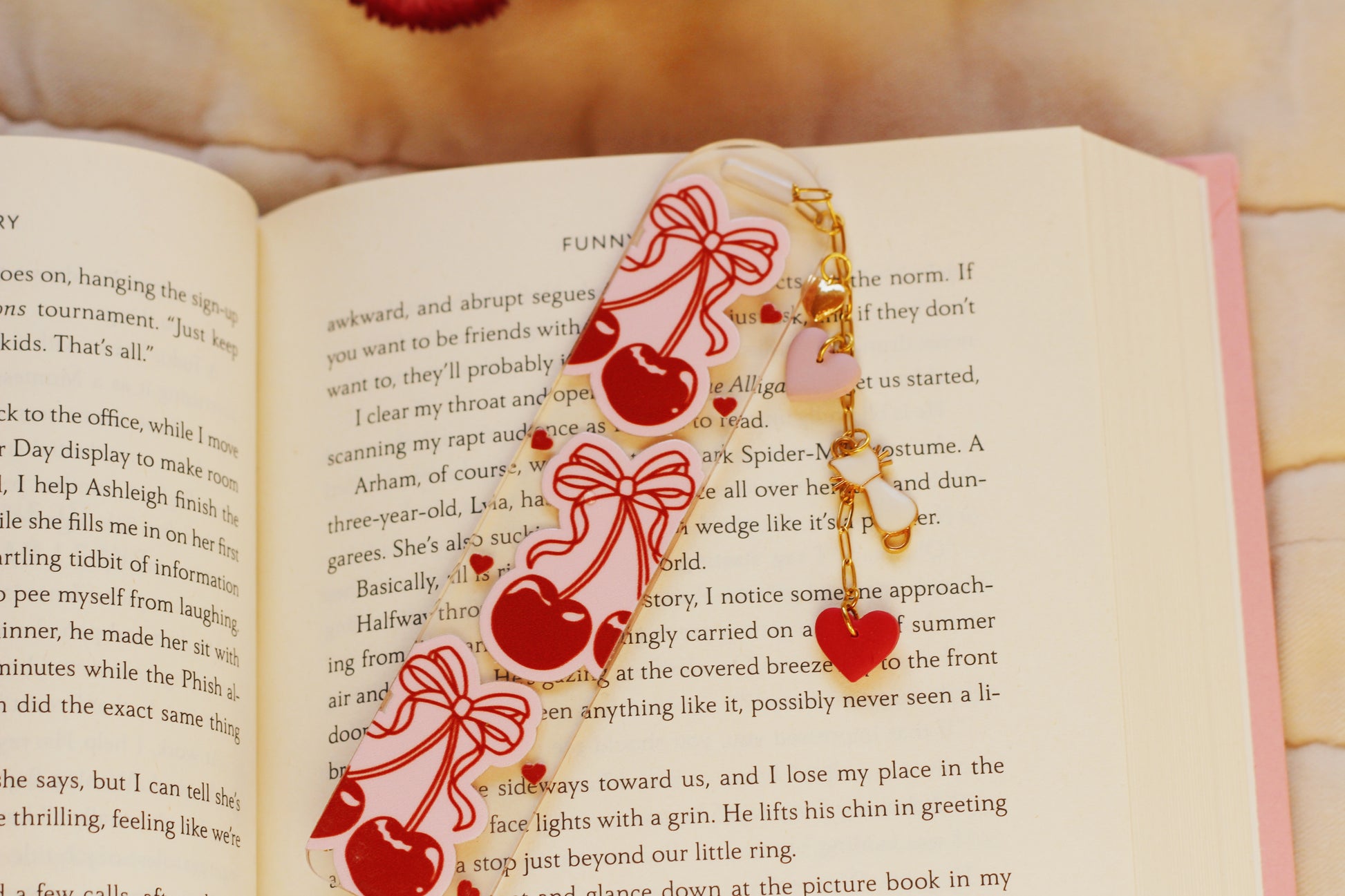 Open book with decorative bookmark featuring cherries and bows on a soft fabric background.