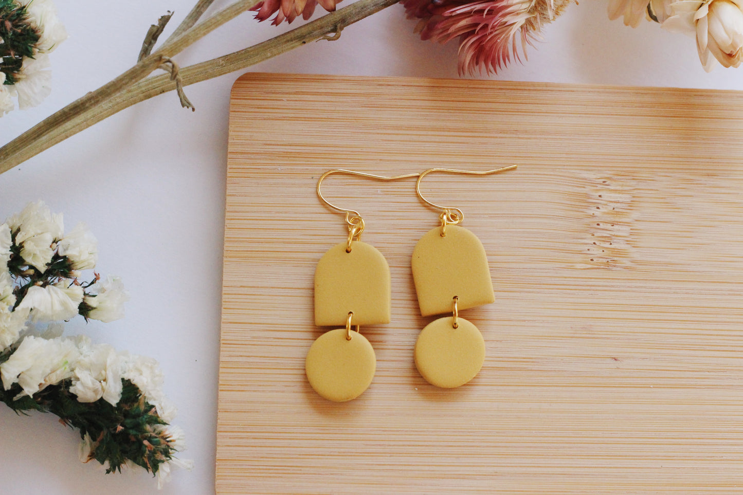 Yellow earrings on a wooden surface with flowers in the background