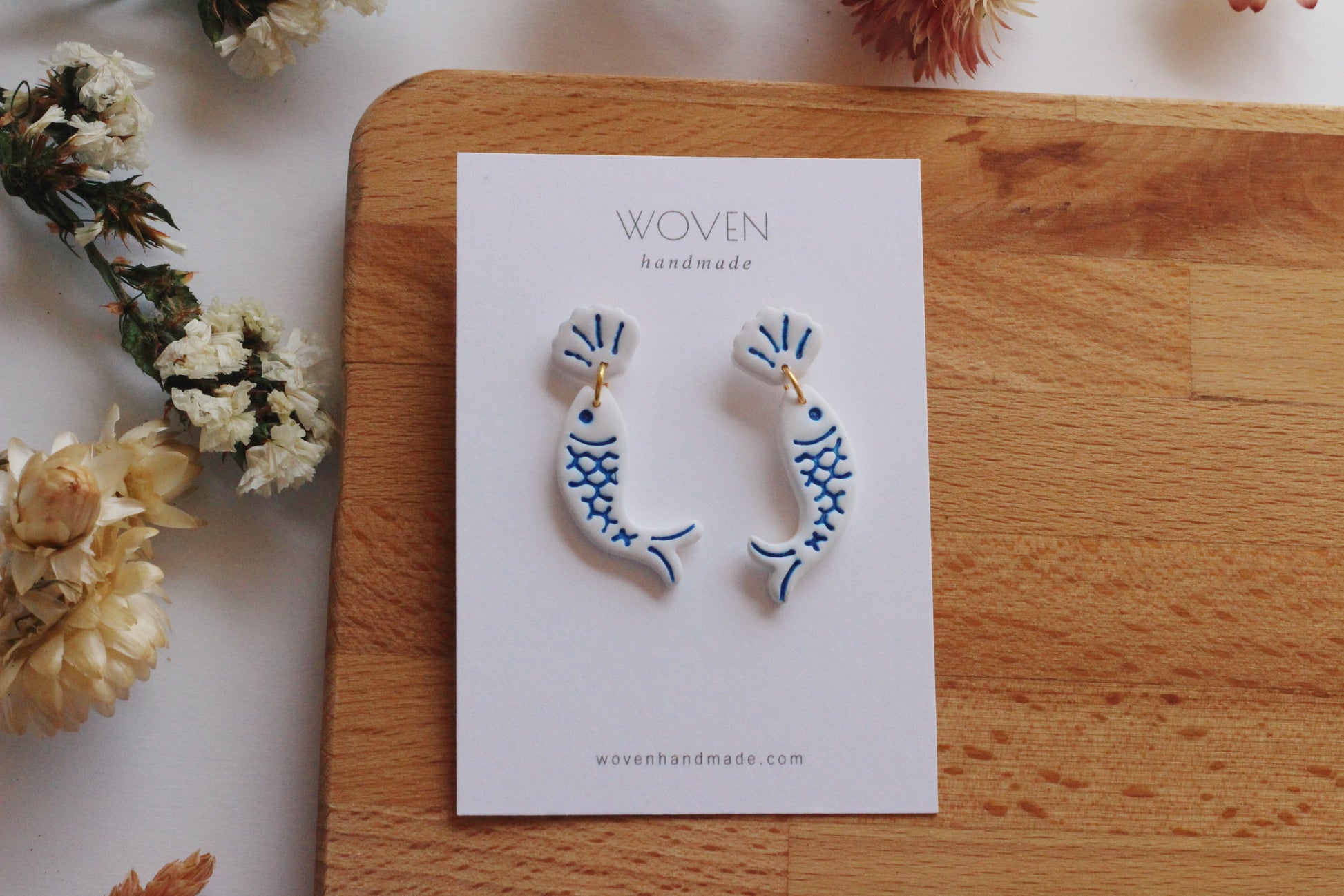 Pair of fish-shaped earrings on a 'Woven Handmade' card with flowers around