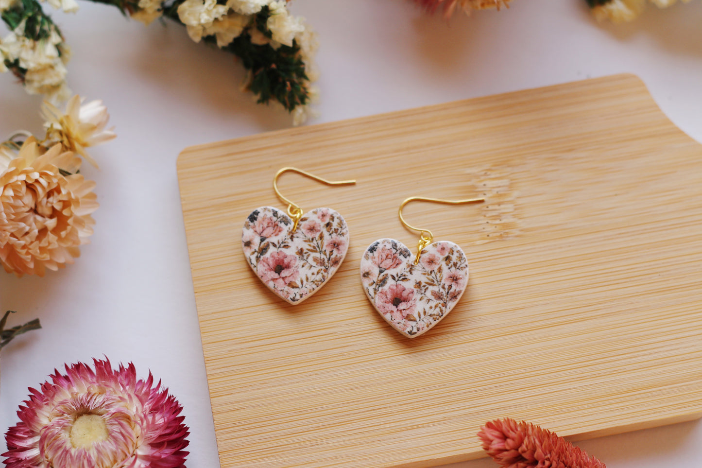 Heart-shaped floral earrings on a wooden board with flowers around