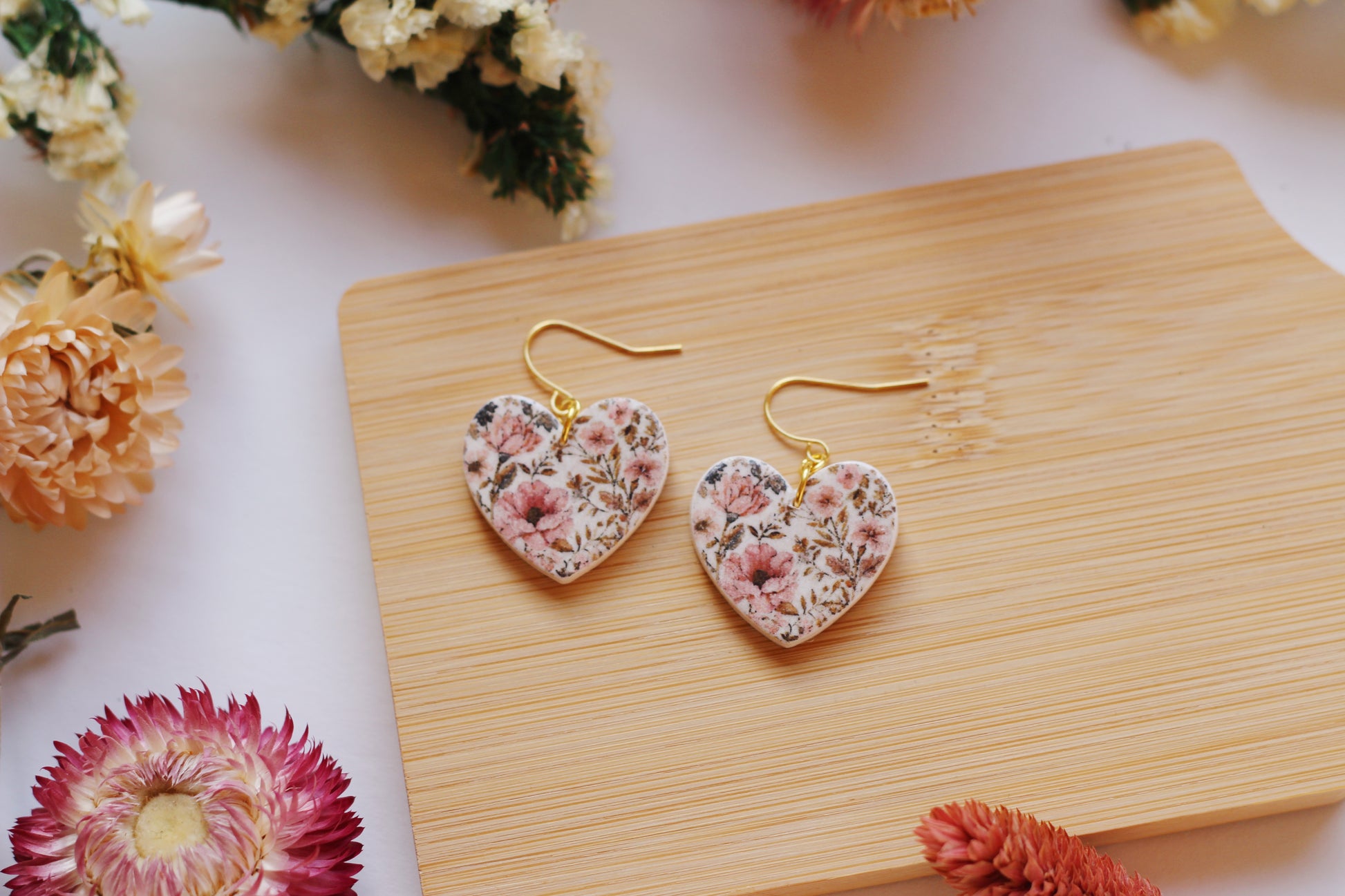 Heart-shaped floral earrings on a wooden board with flowers around