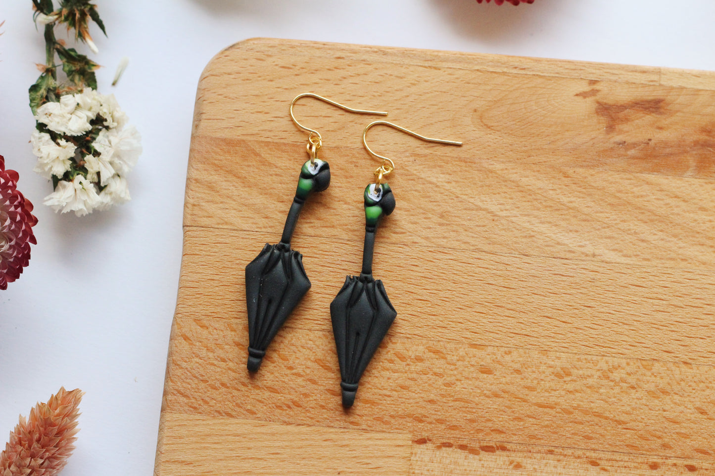 Black and gold earrings on a wooden board with flowers in the background