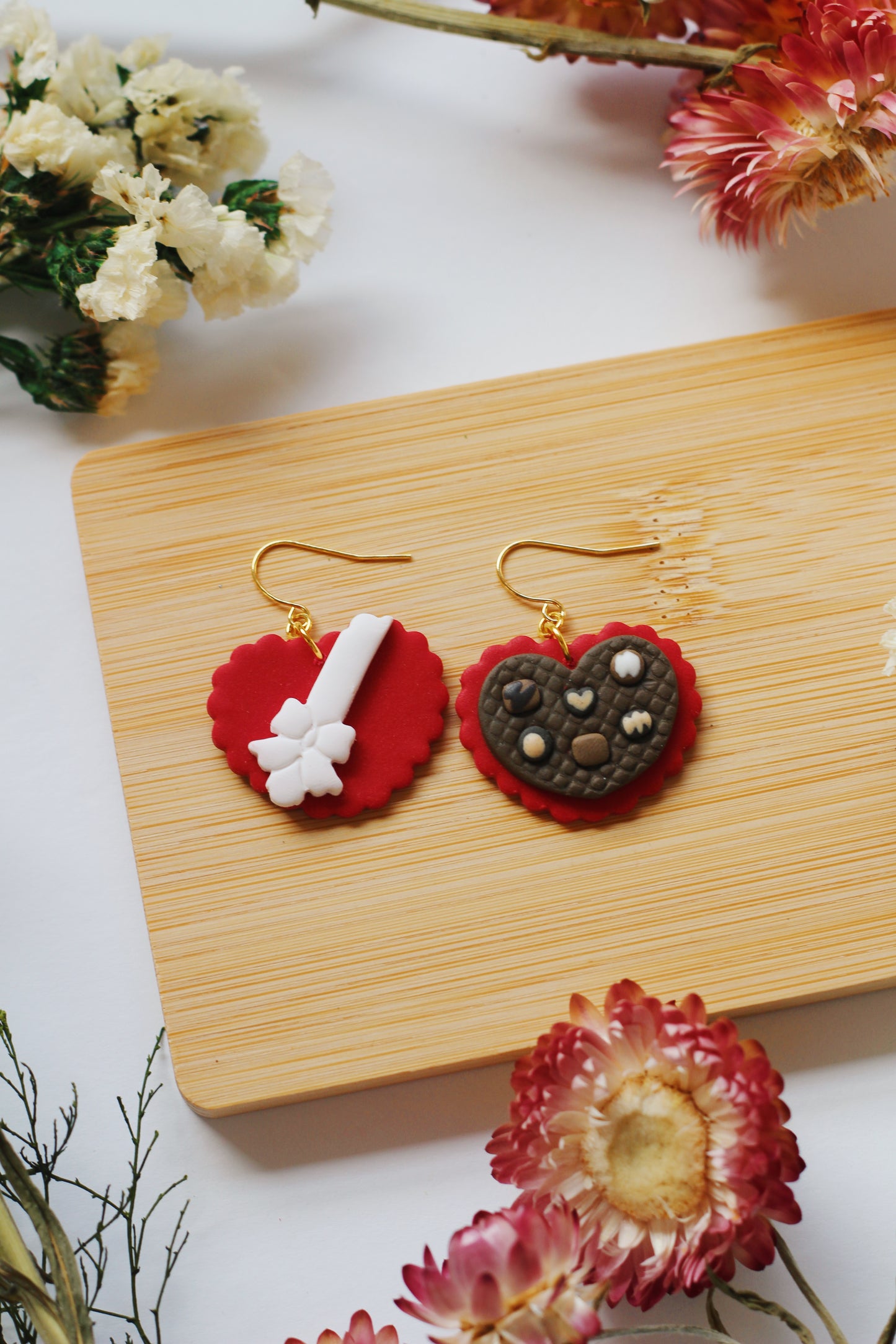 Heart-shaped chocolate box earrings on a wooden board with flowers around