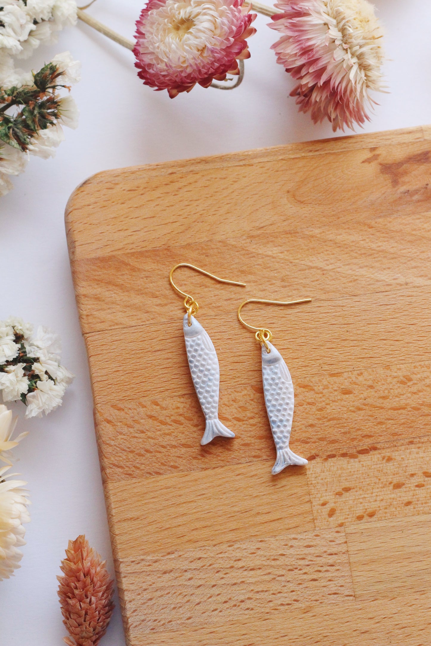 Fish-shaped earrings on a wooden board with flowers in the background