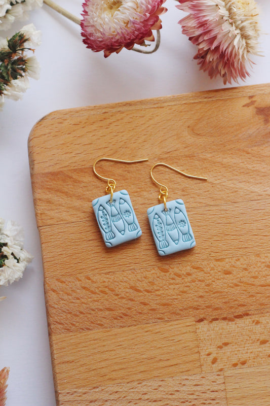 Pair of light blue earrings on a wooden surface with flowers in the background