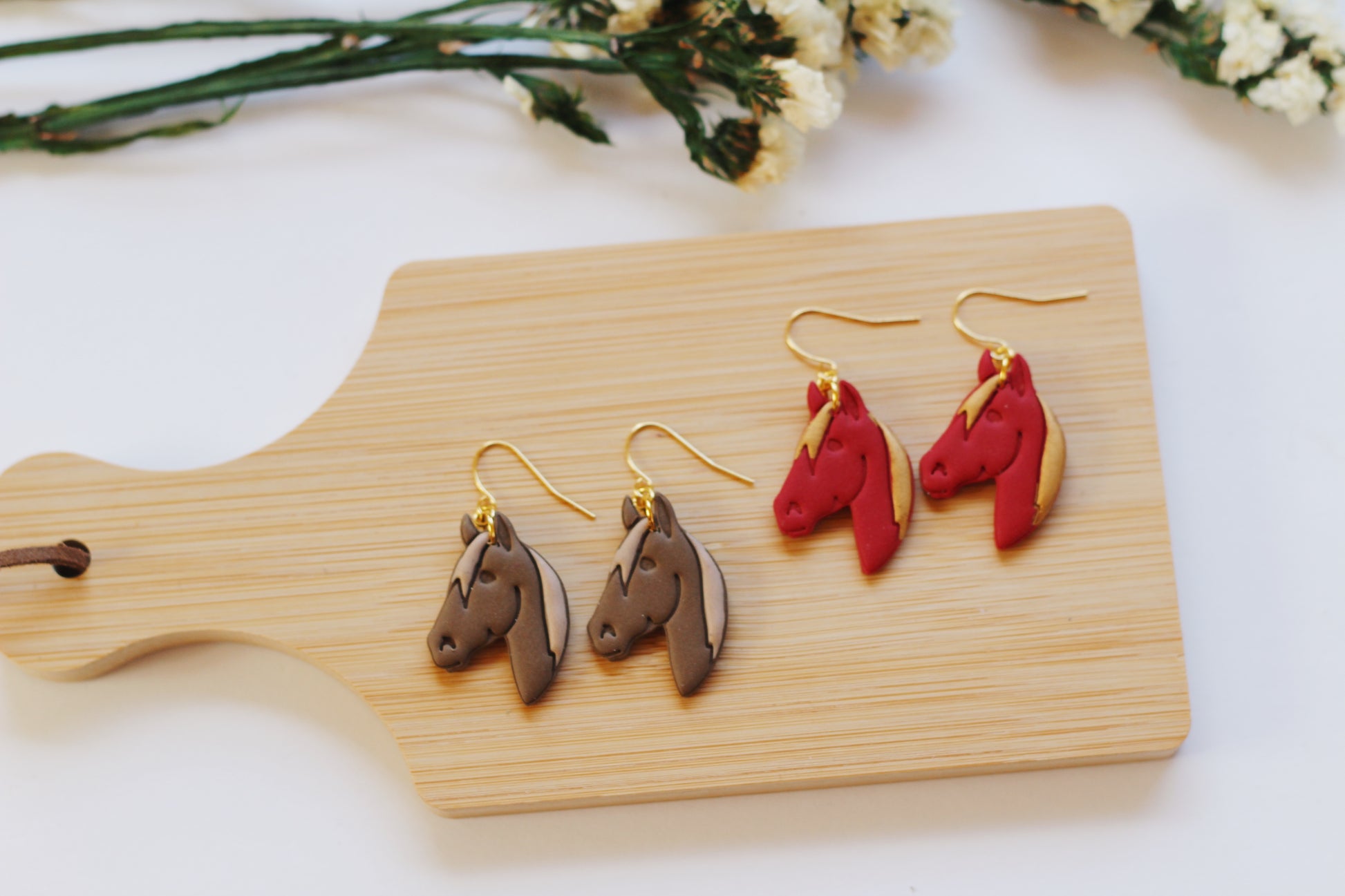 Horse-shaped earrings on a wooden board with flowers in the background
