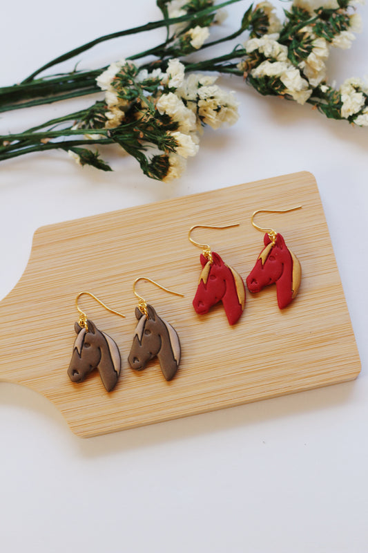Horse-shaped earrings on a wooden board with flowers in the background