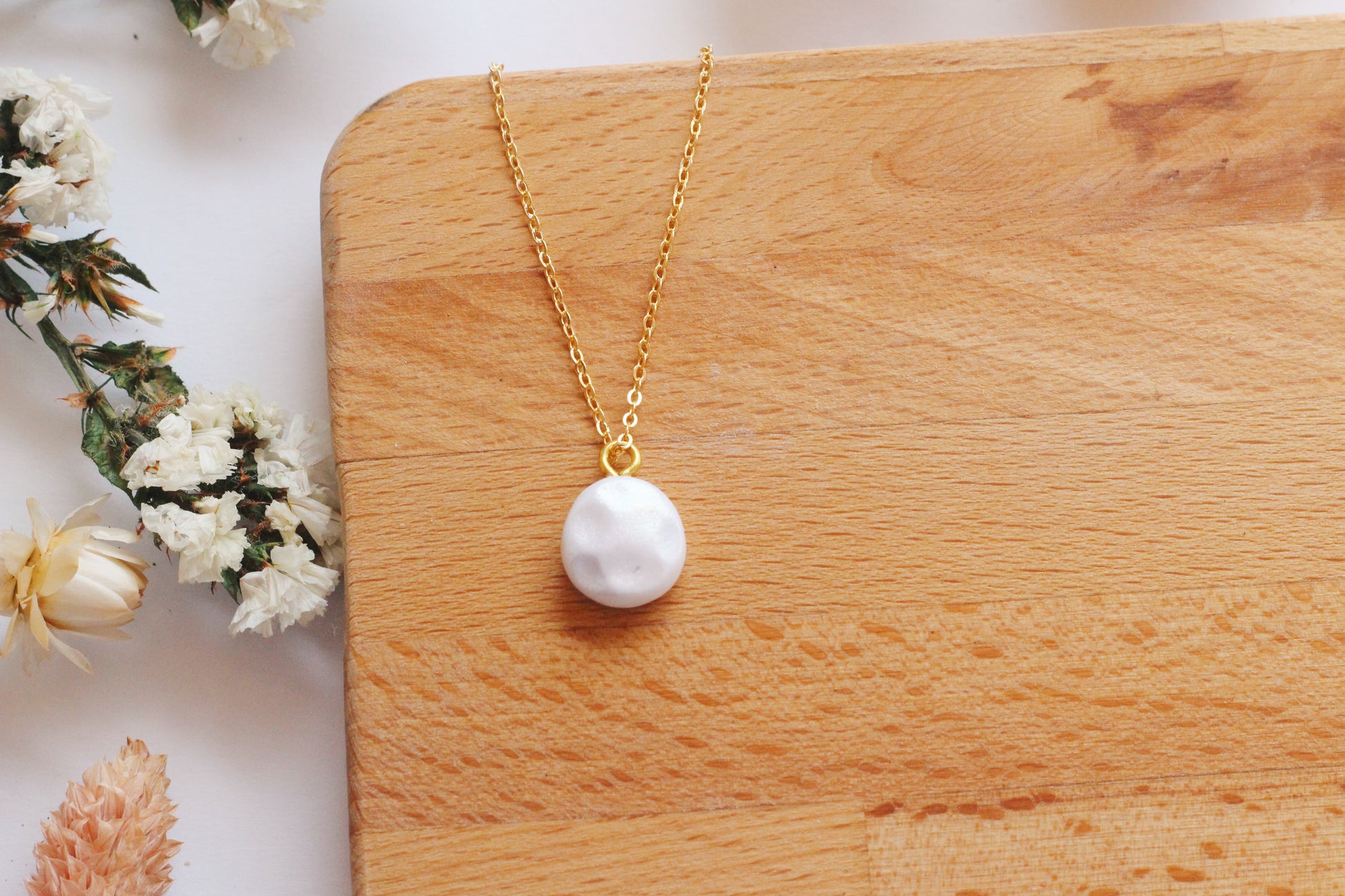 Gold necklace with a faux pearl pendant on a wooden surface with flowers in the background