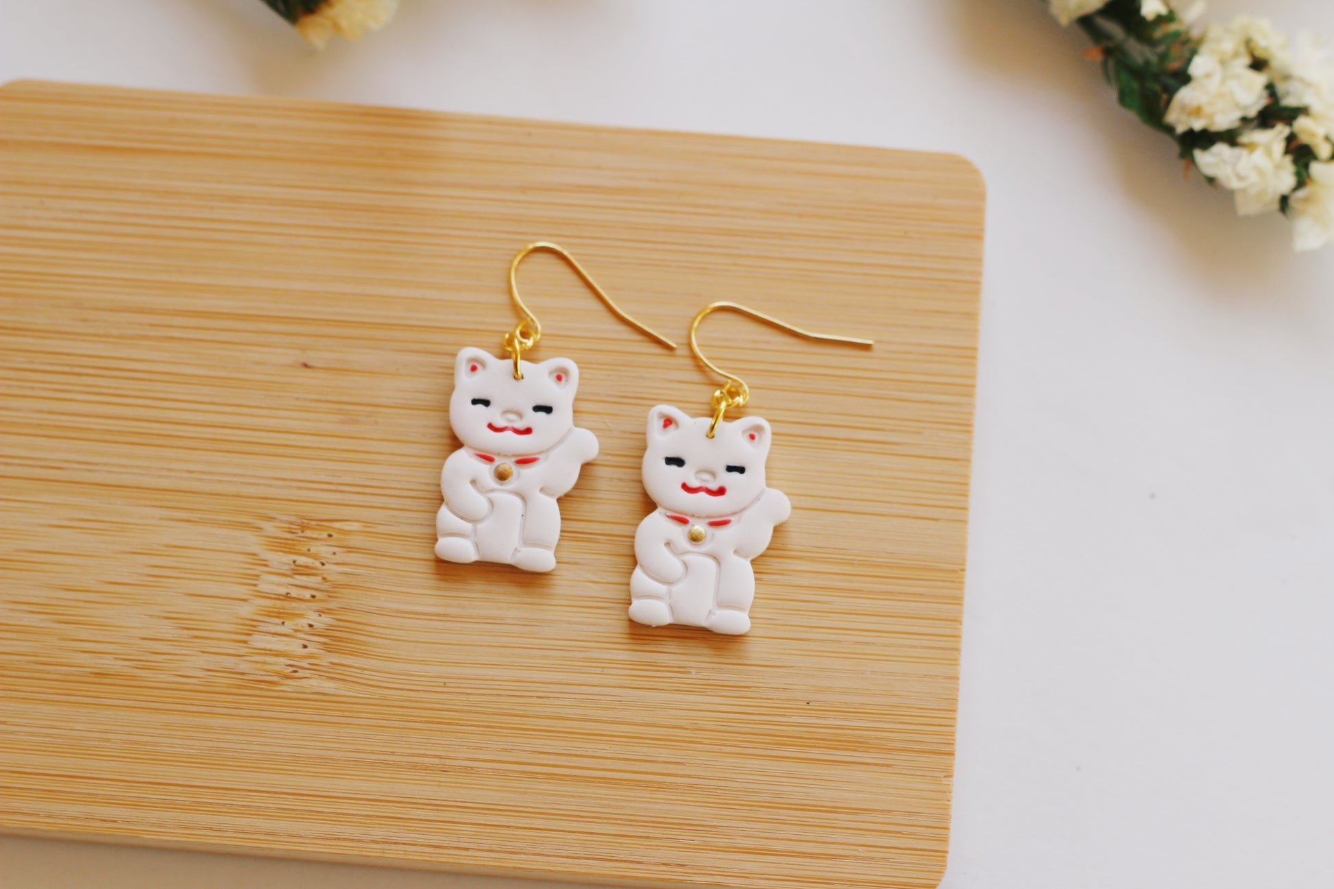 White cat-shaped earrings with gold hooks on a wooden surface.