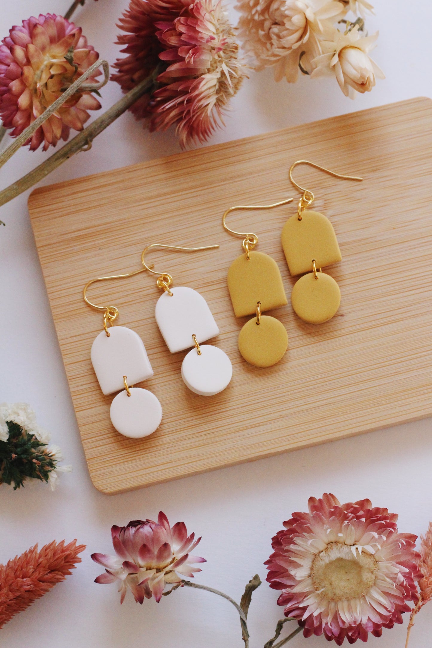 Pair of yellow and white earrings on a wooden board with flowers around.