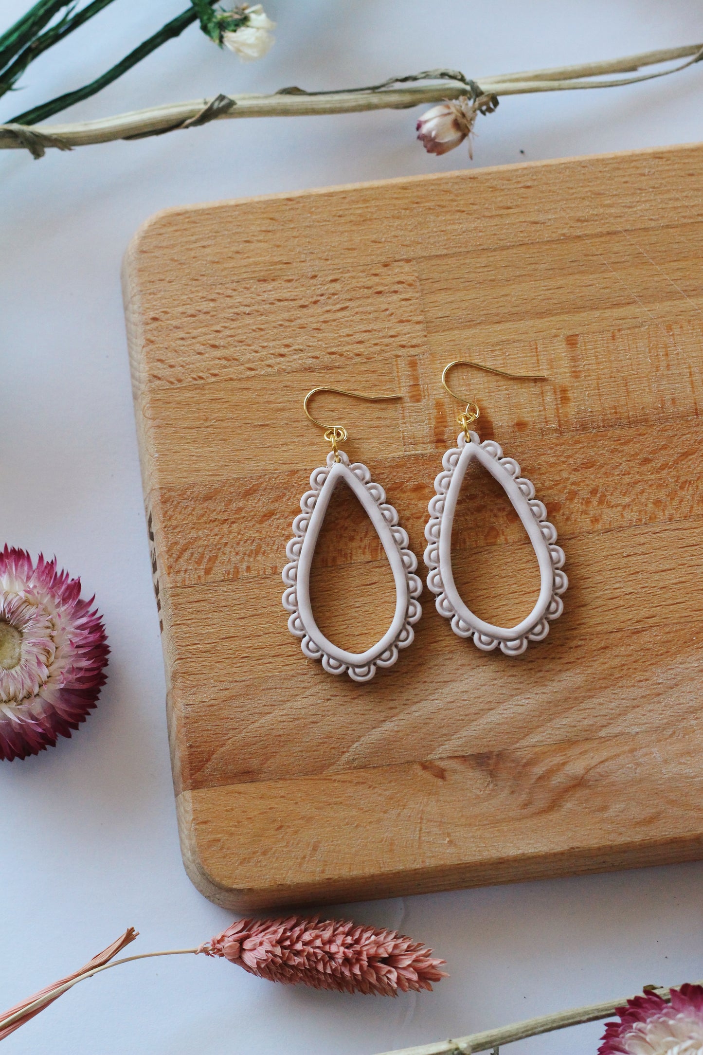 Pair of white hoop earrings on a wooden block with dried flowers around.