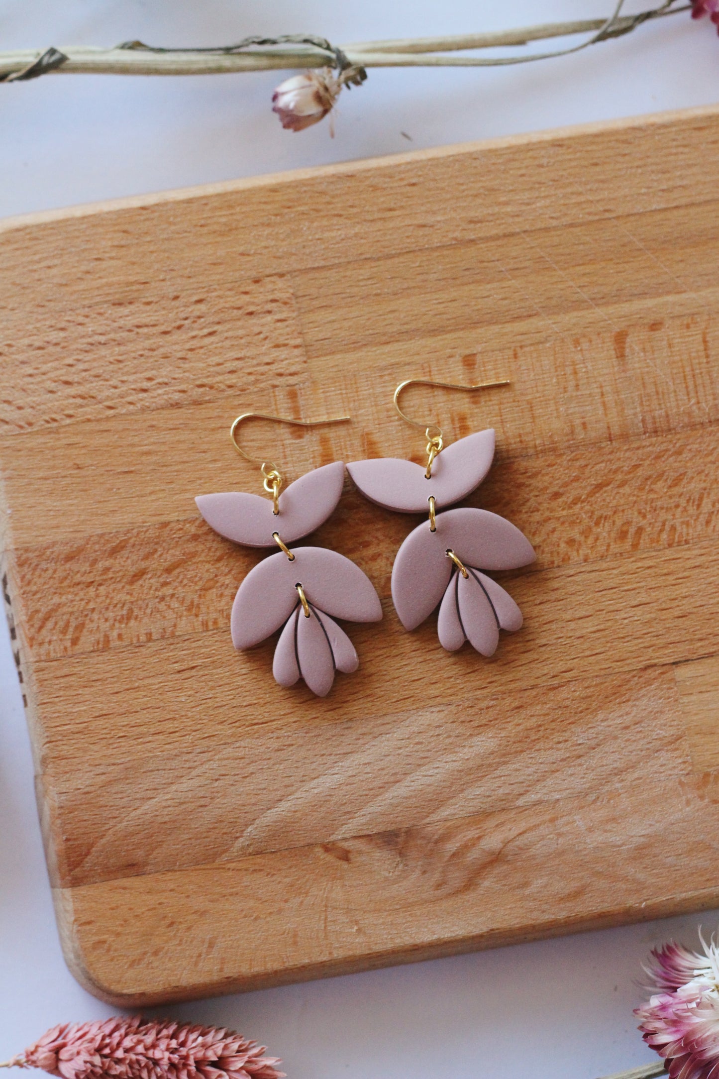 Pink floral earrings on a wooden board with dried flowers.