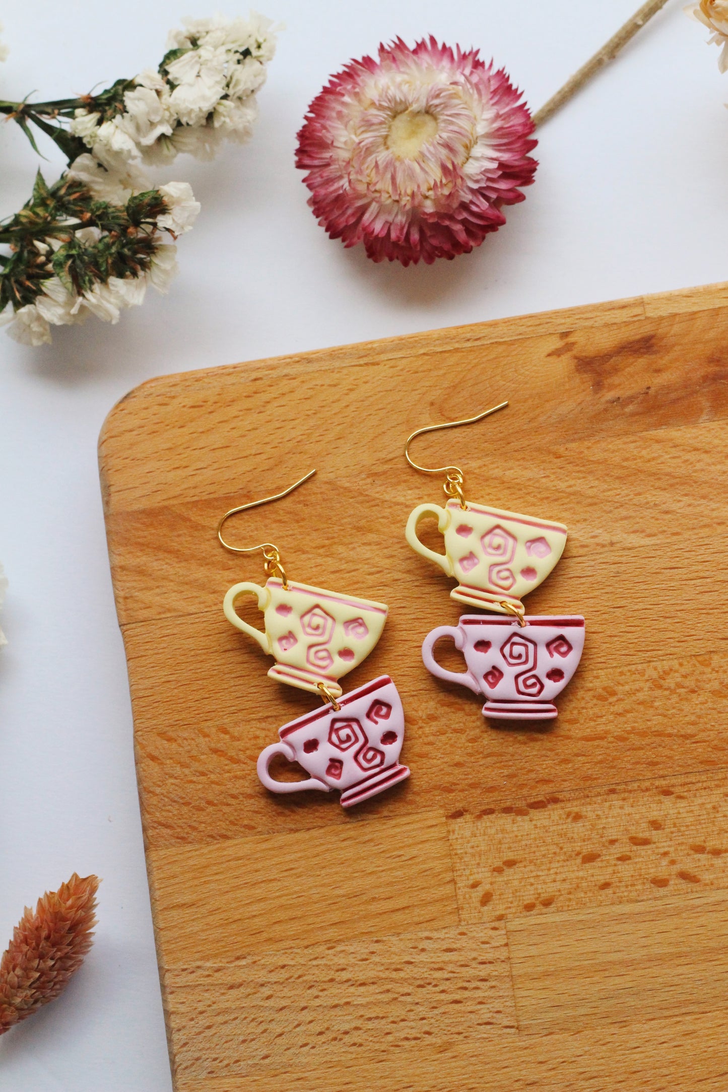 Teacup-shaped earrings on a wooden board with flowers in the background