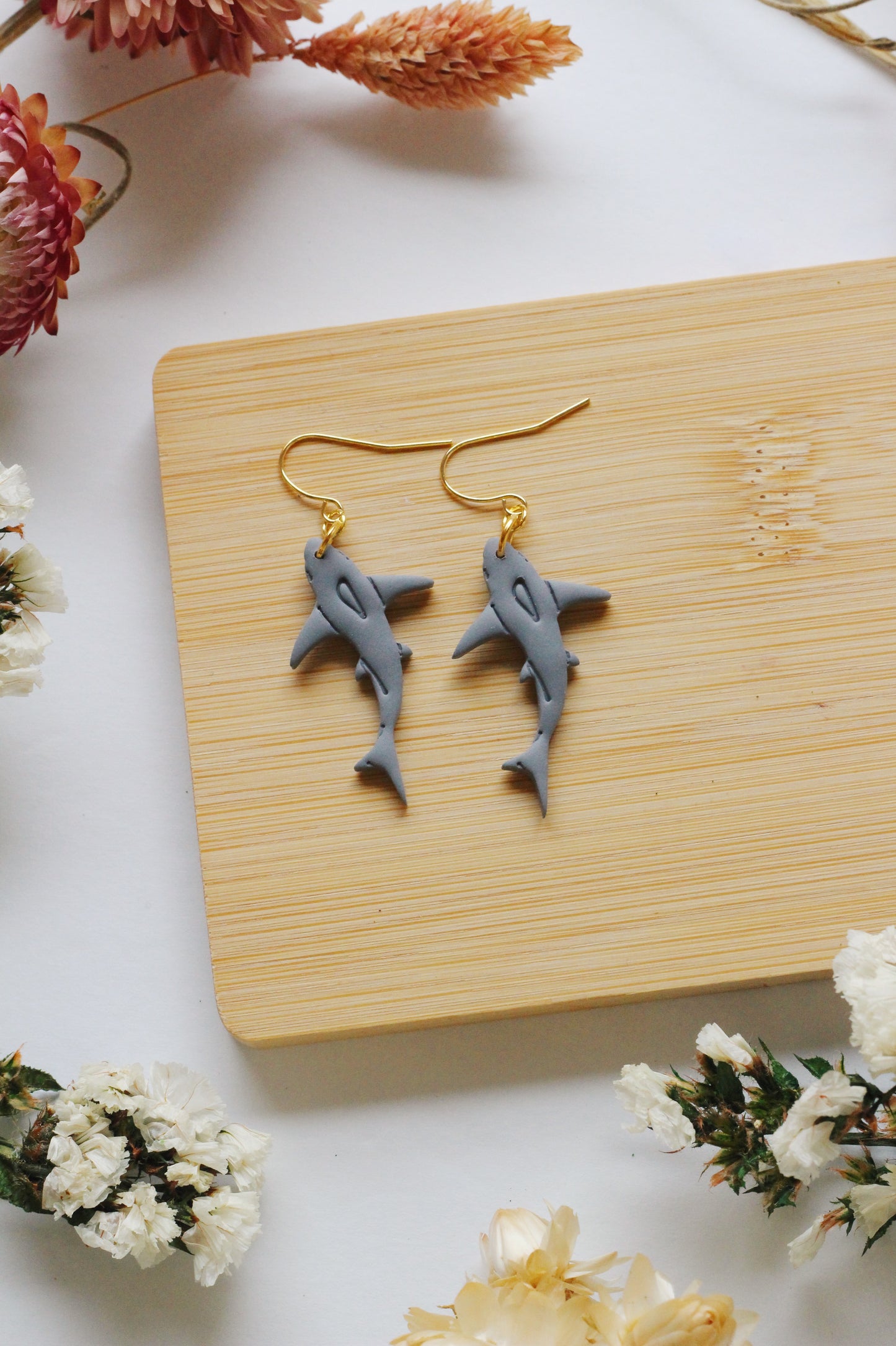 Shark-shaped earrings on a wooden board with flowers around