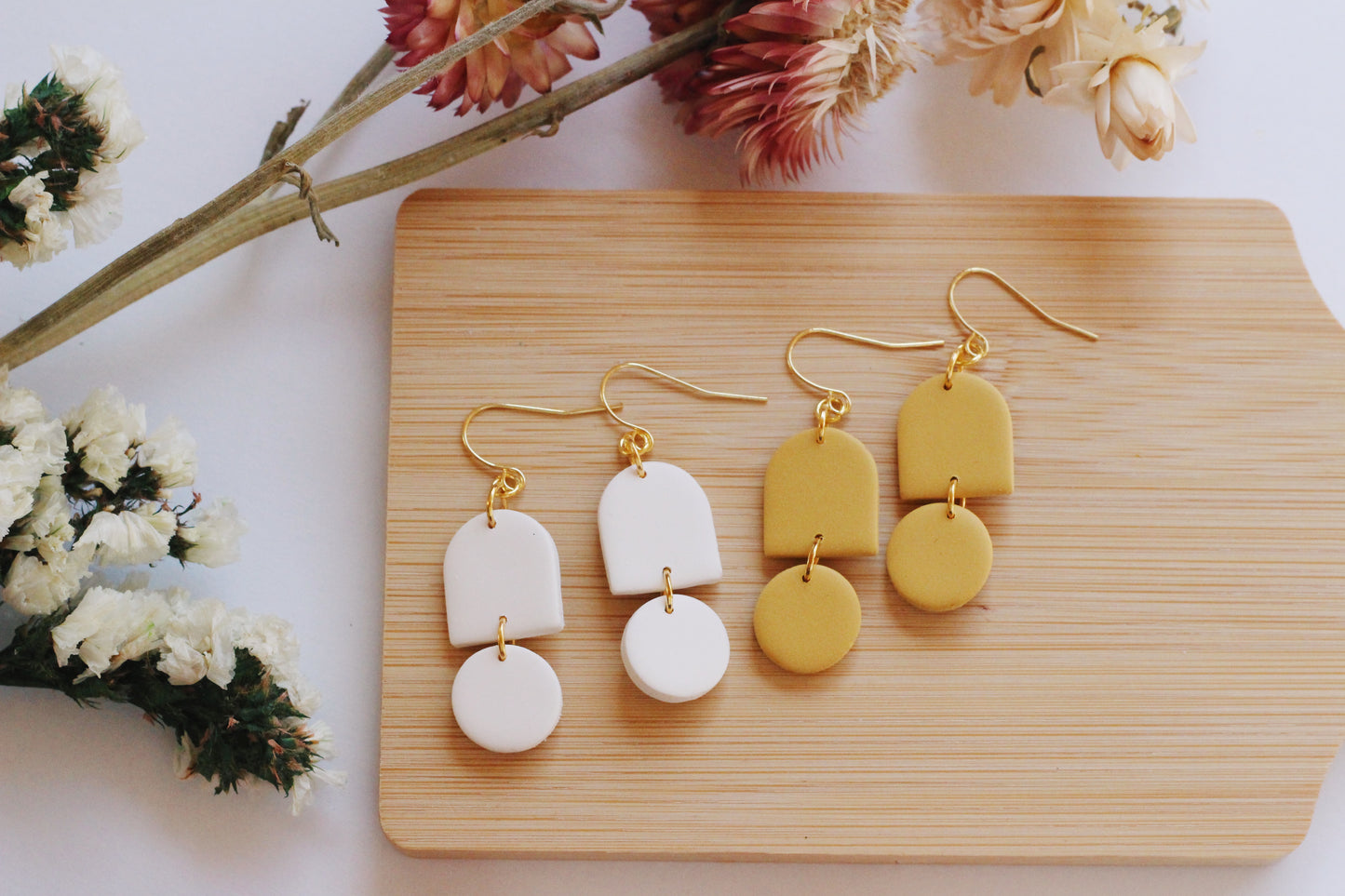Pair of gold and yellow earrings on a wooden board with flowers in the background