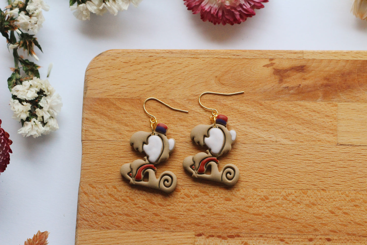 Monkey earrings on a wooden board with flowers in the background