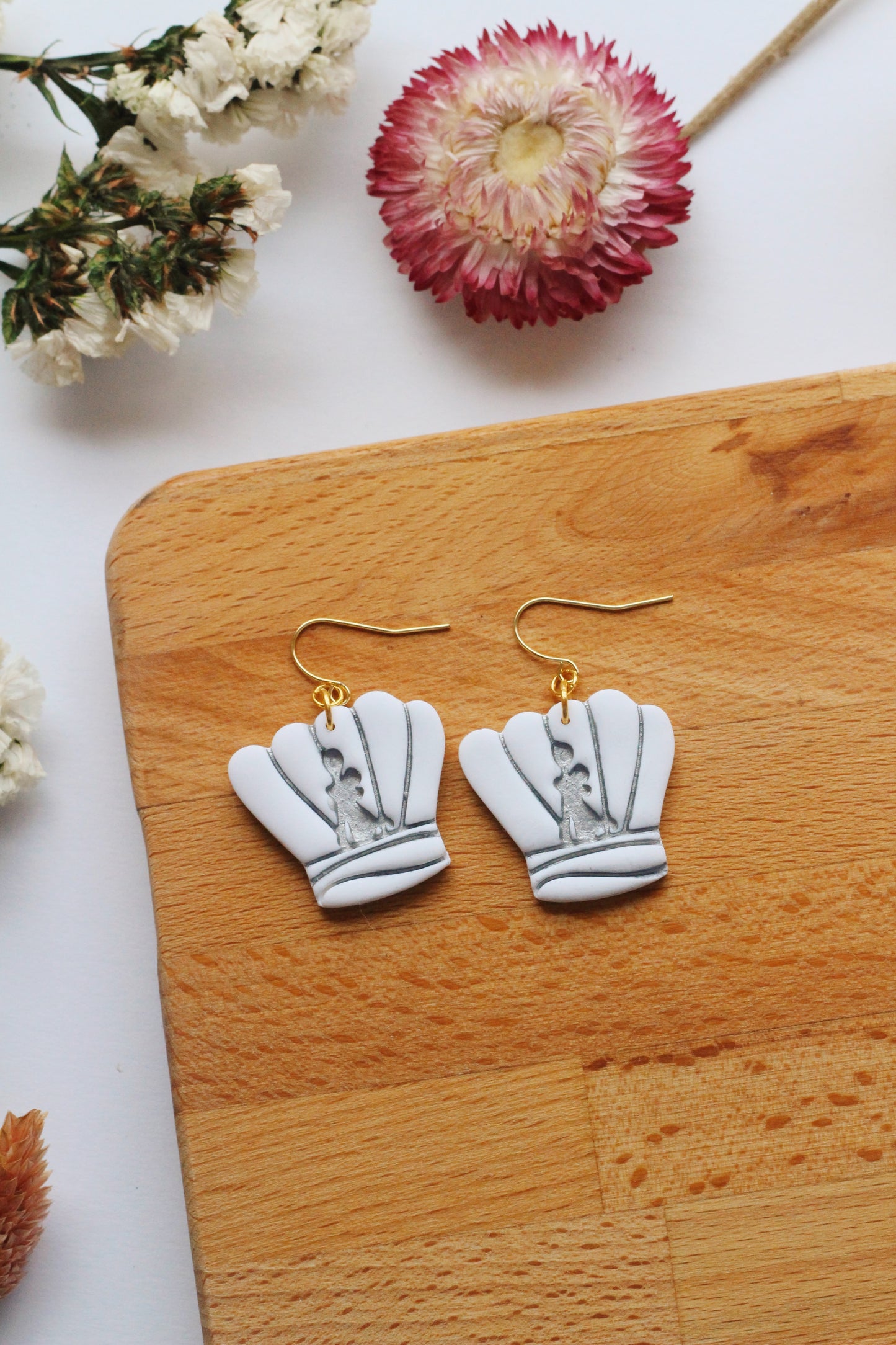 Chef hat earrings on a wooden board with flowers in the background