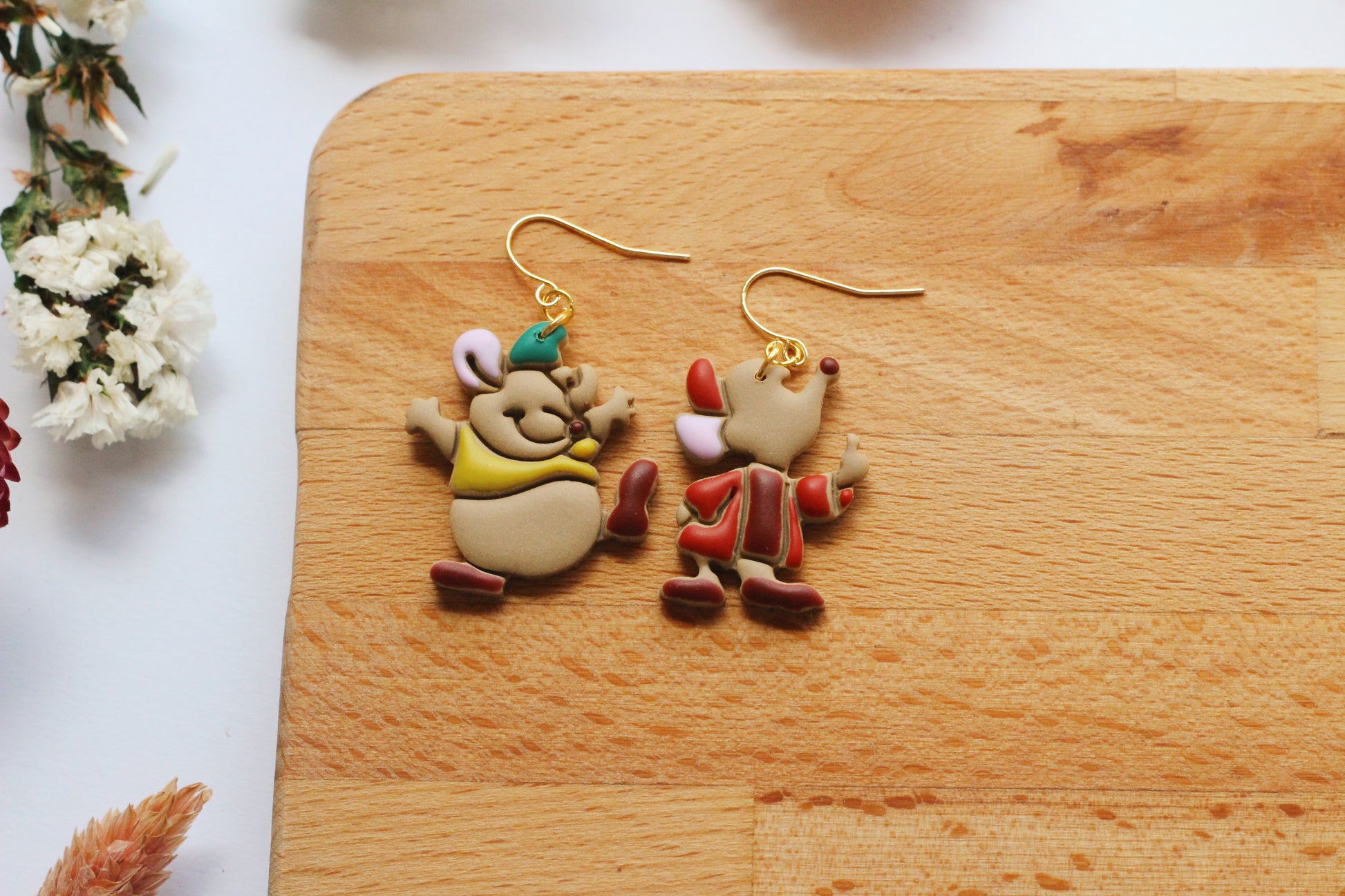 Two cartoon-style earrings on a wooden board with flowers in the background