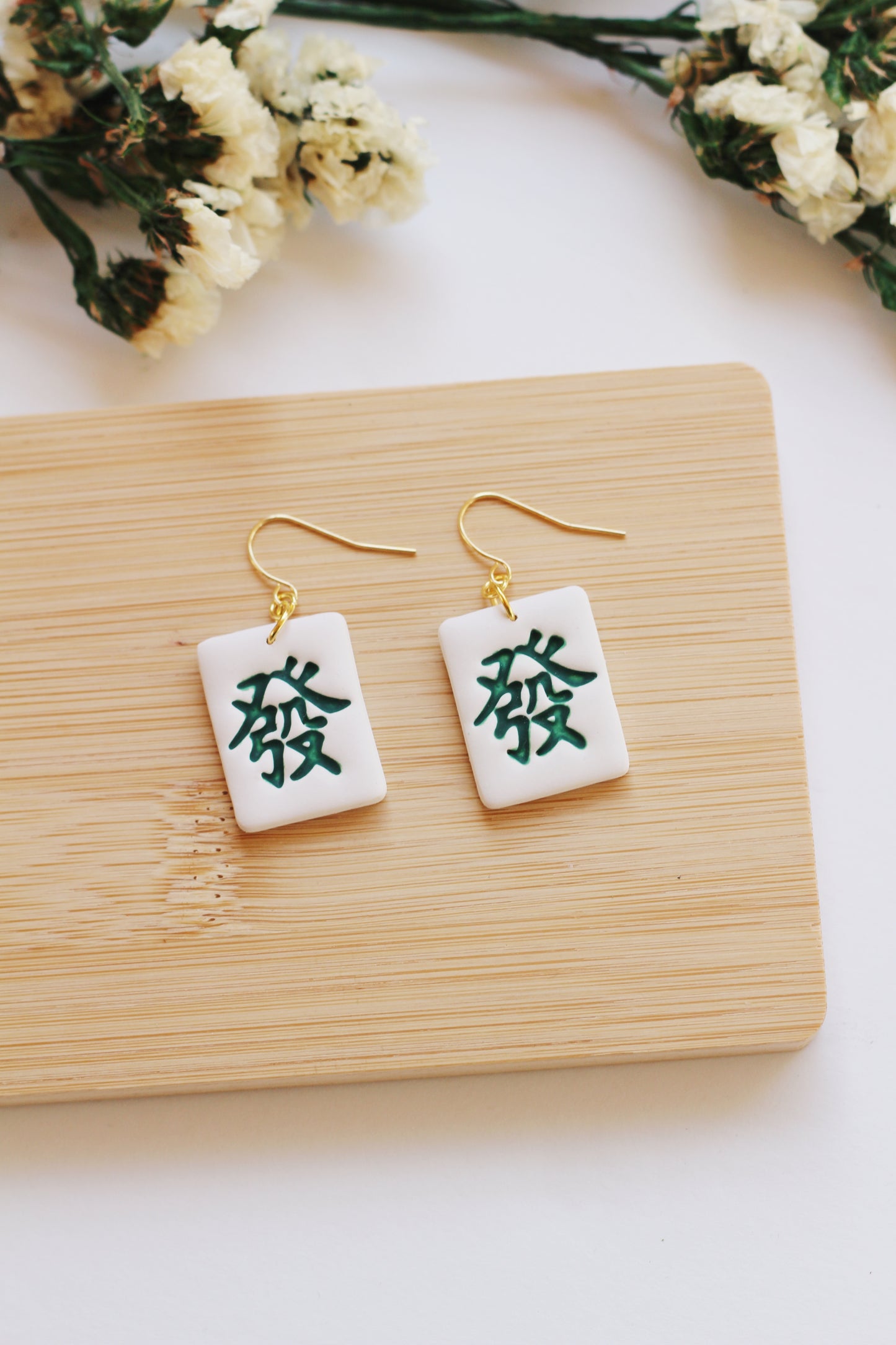 Pair of earrings with green dragon mahjong tile style, displayed on a wooden board