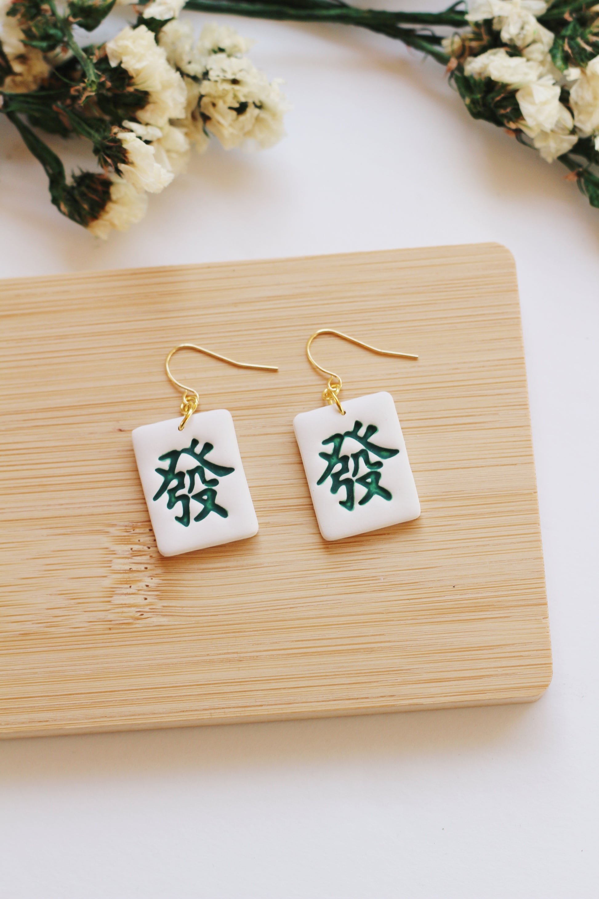 Pair of earrings with green dragon mahjong tile style, displayed on a wooden board