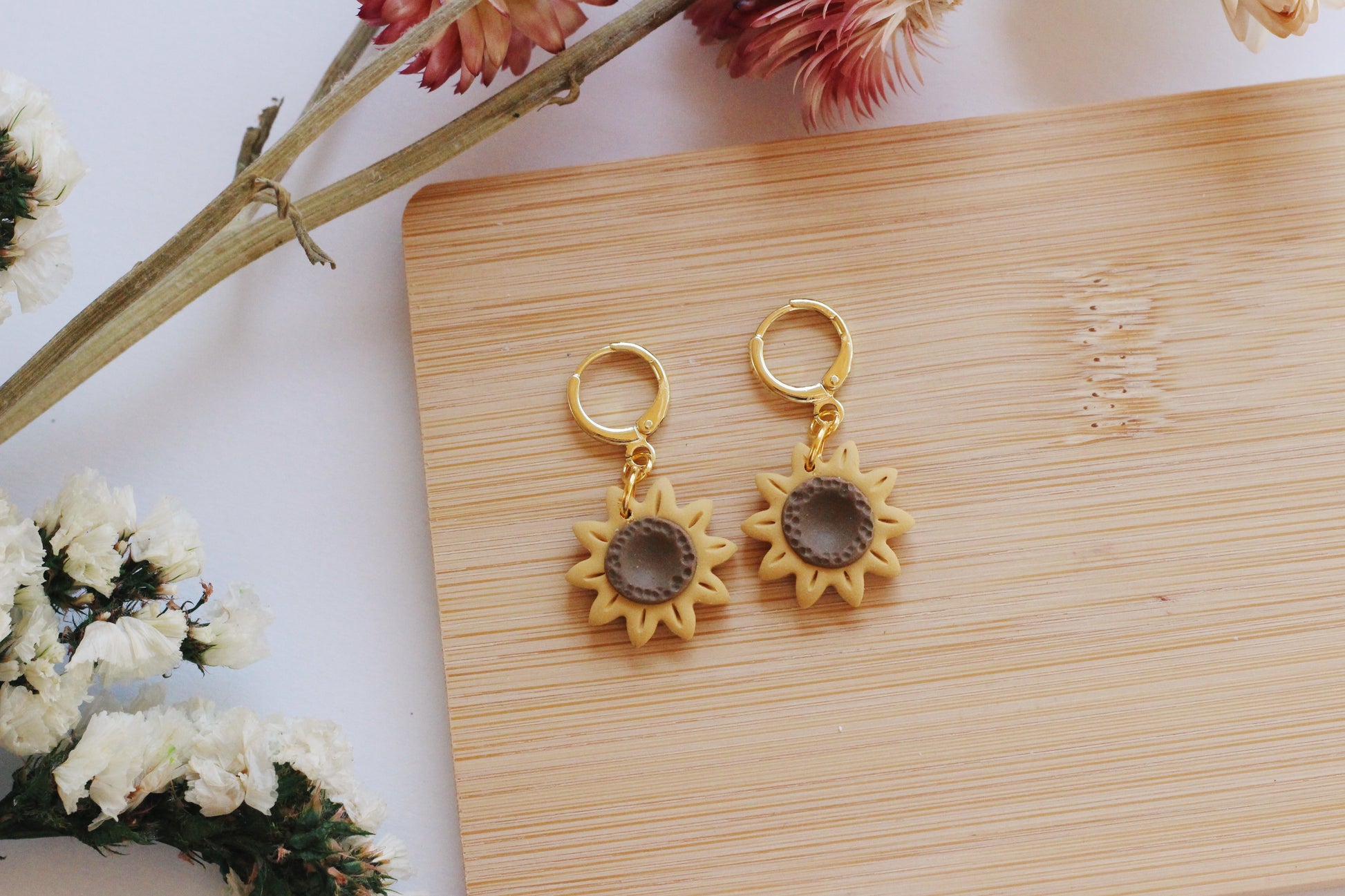 Sun-shaped earrings on a wooden board with flowers in the background