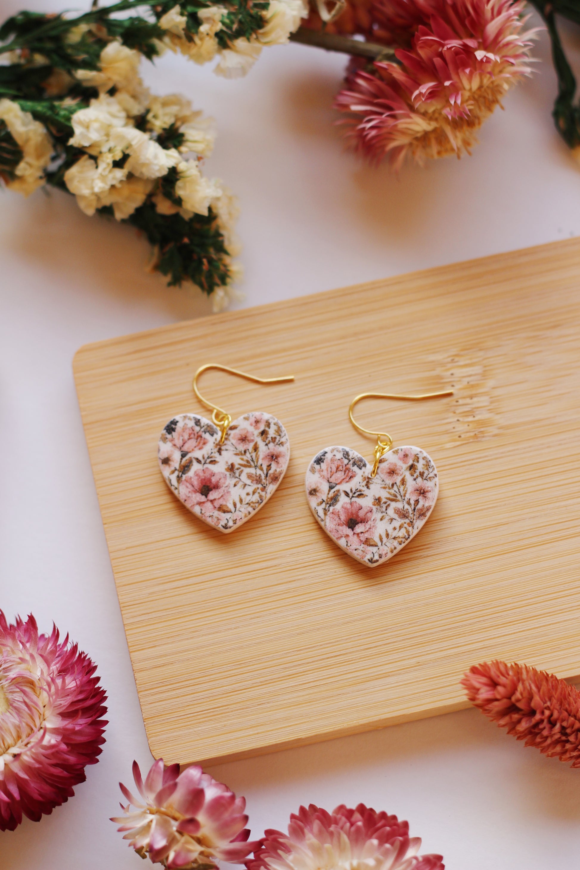 Heart-shaped floral earrings on a wooden stand with flowers around