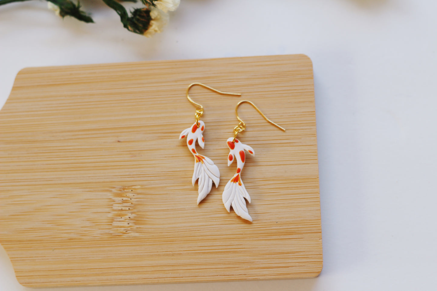 Gold and white fish-shaped earrings on a wooden board with a white background