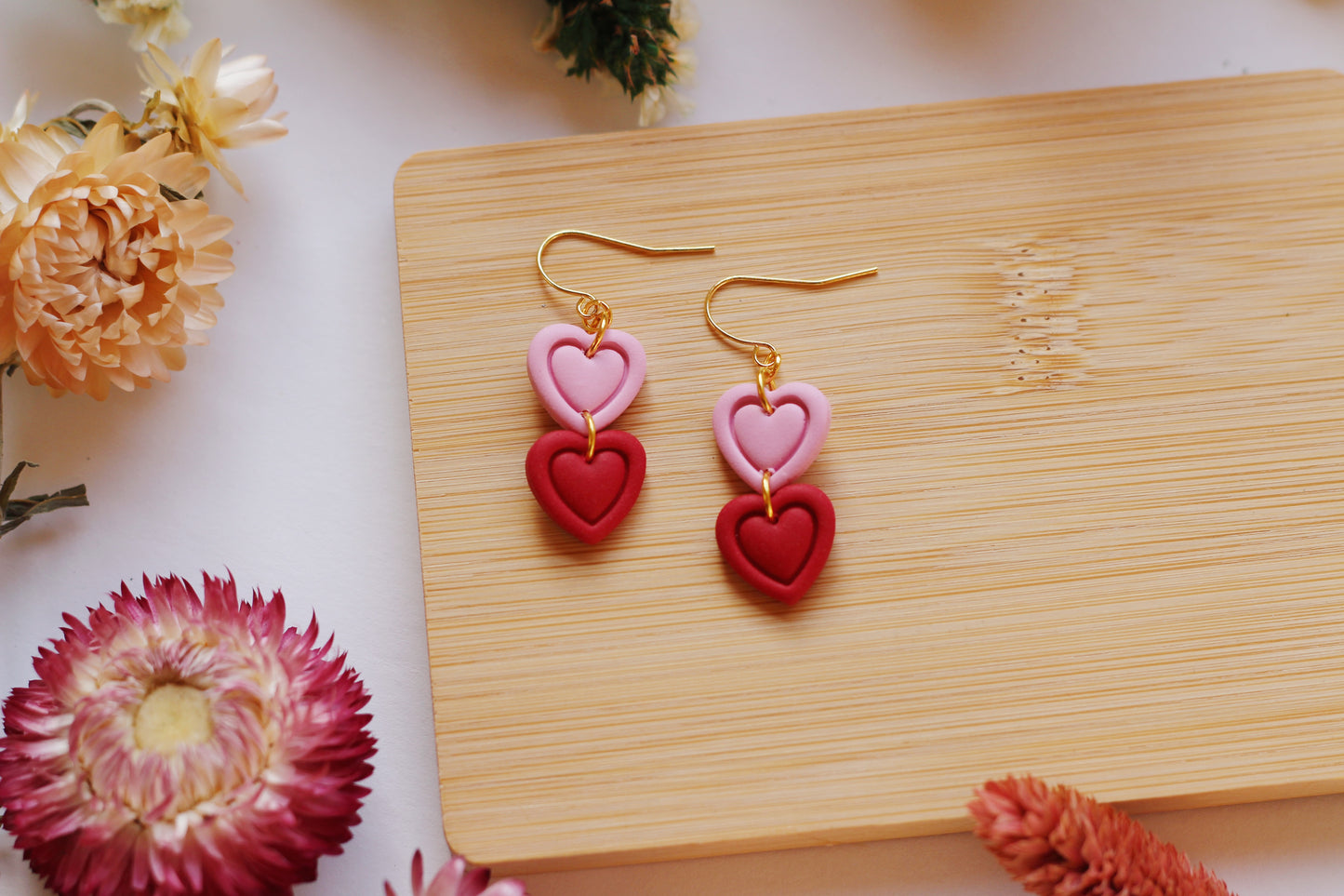 Heart-shaped earrings on a wooden board with flowers around