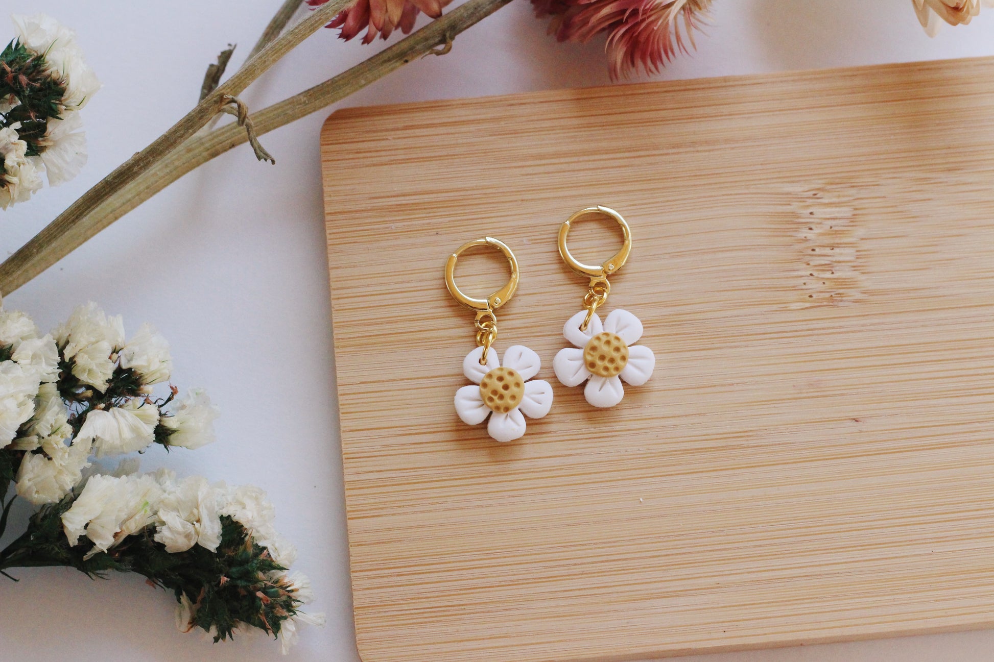 Flower-shaped earrings on a wooden board with flowers around