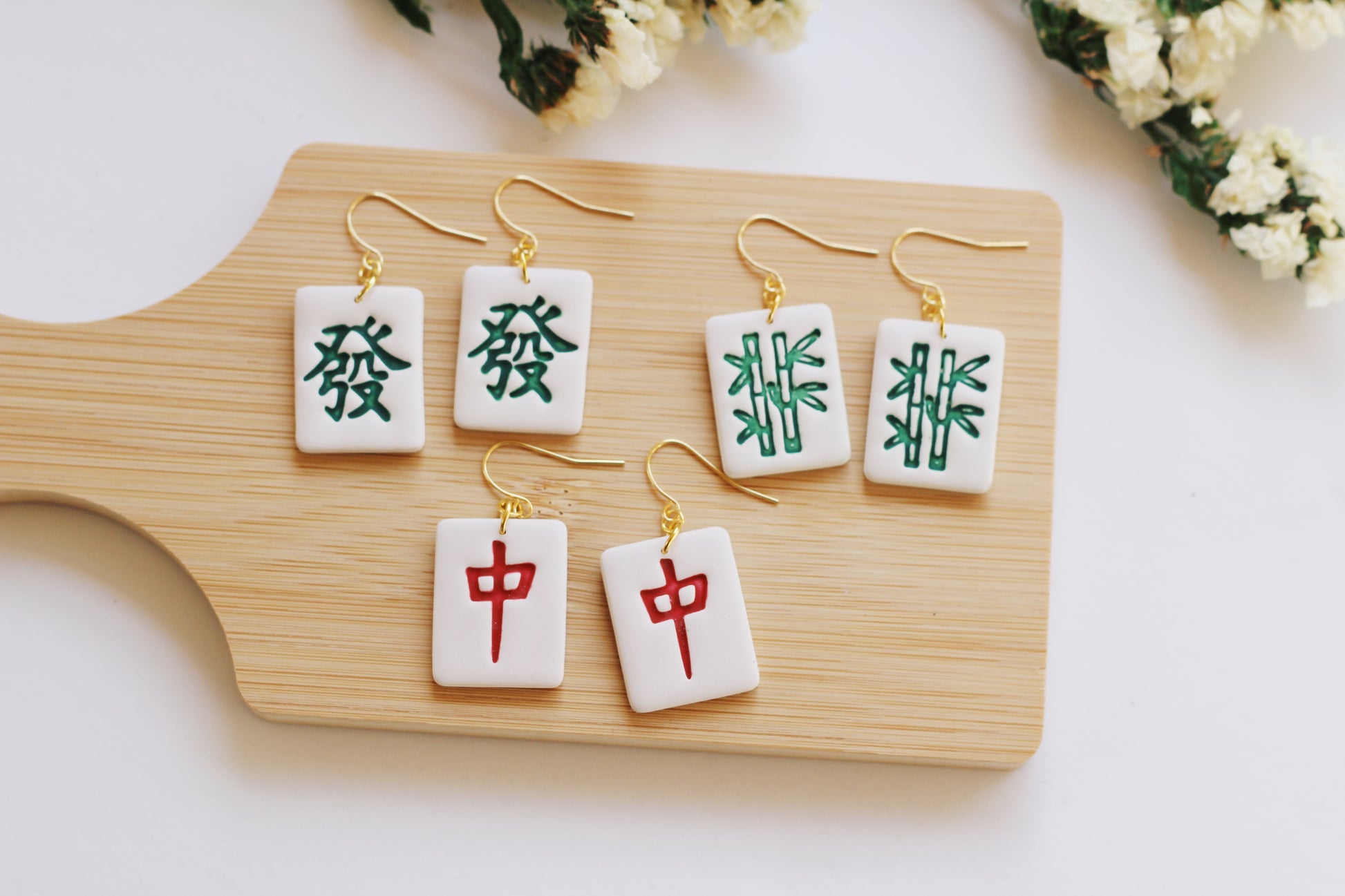 Mandarin Mahjong-themed earrings on a wooden board with flowers in the background