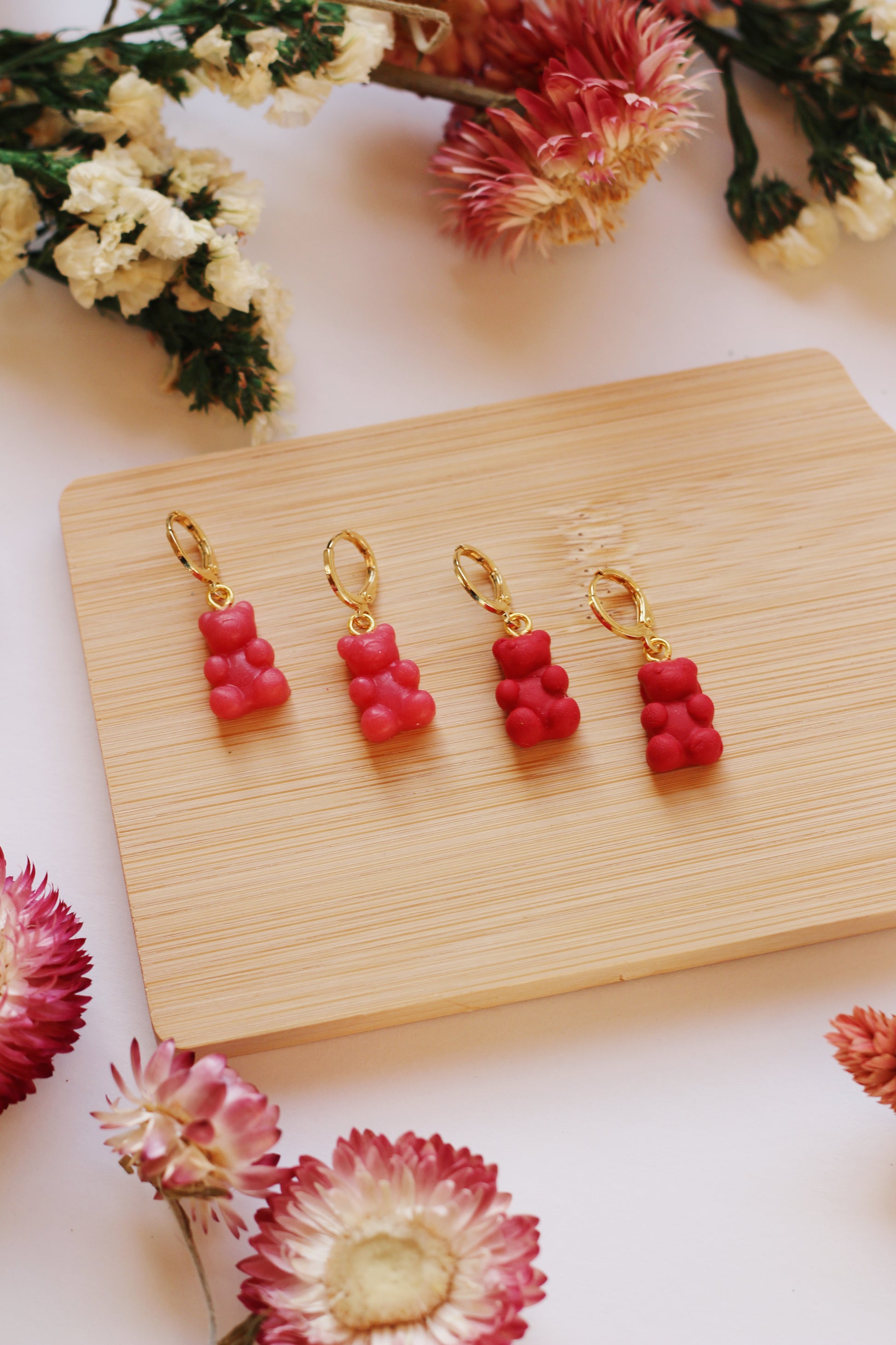 Gummy bear-shaped earrings on a wooden display with flowers around.