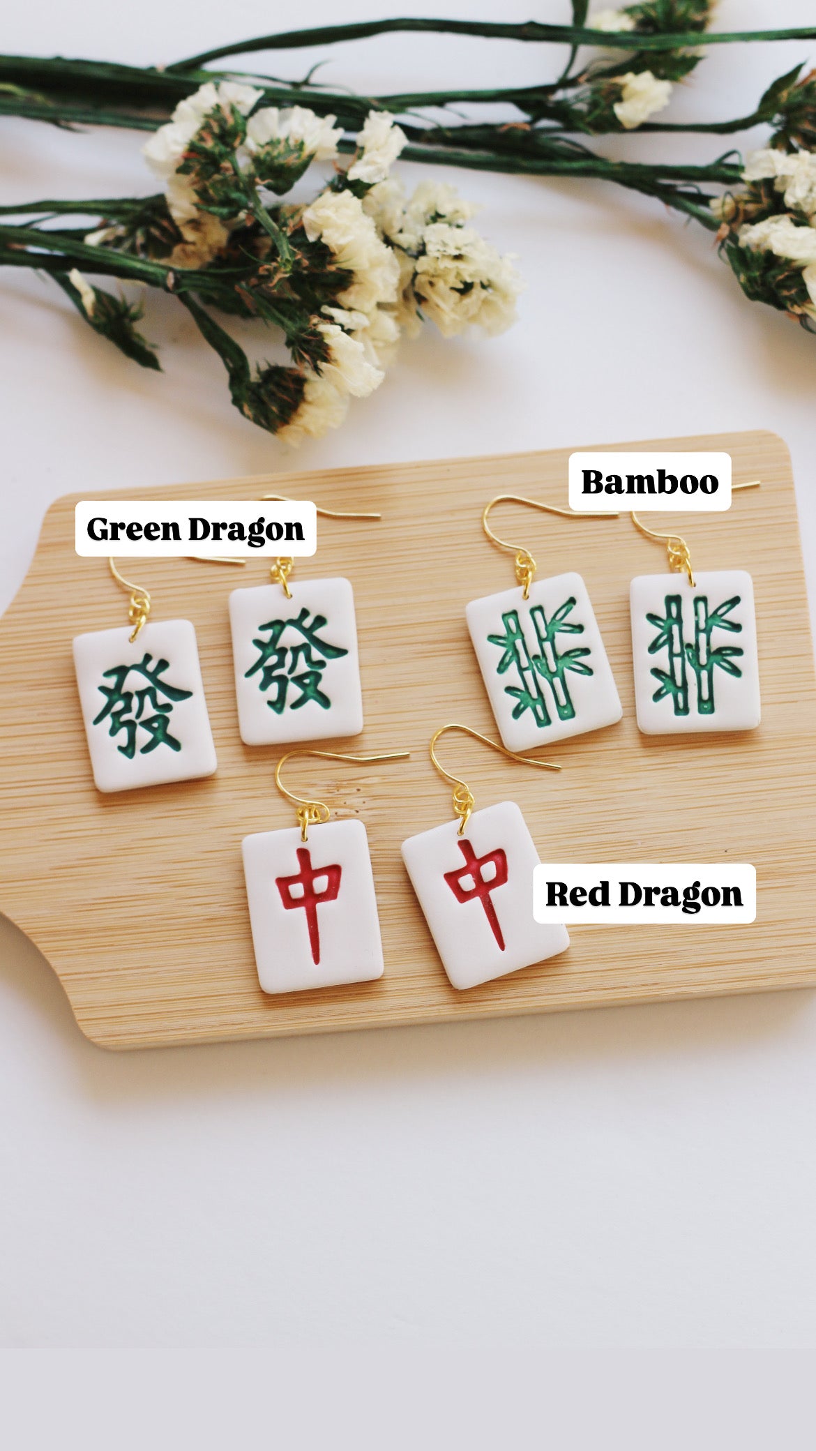 Set of earrings with Chinese characters on a wooden board with white flowers in the background.