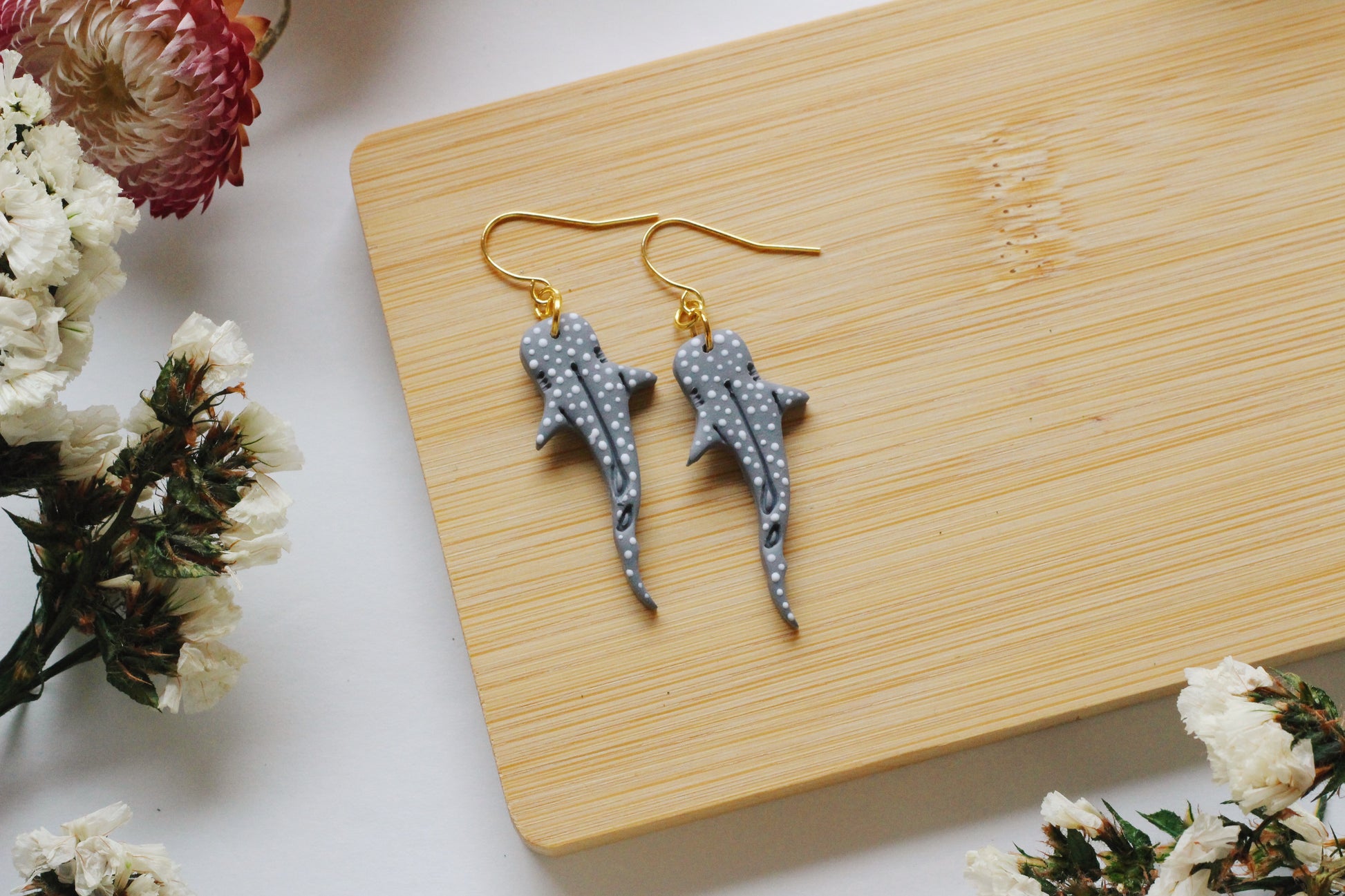 Shark-shaped earrings on a wooden board with flowers around