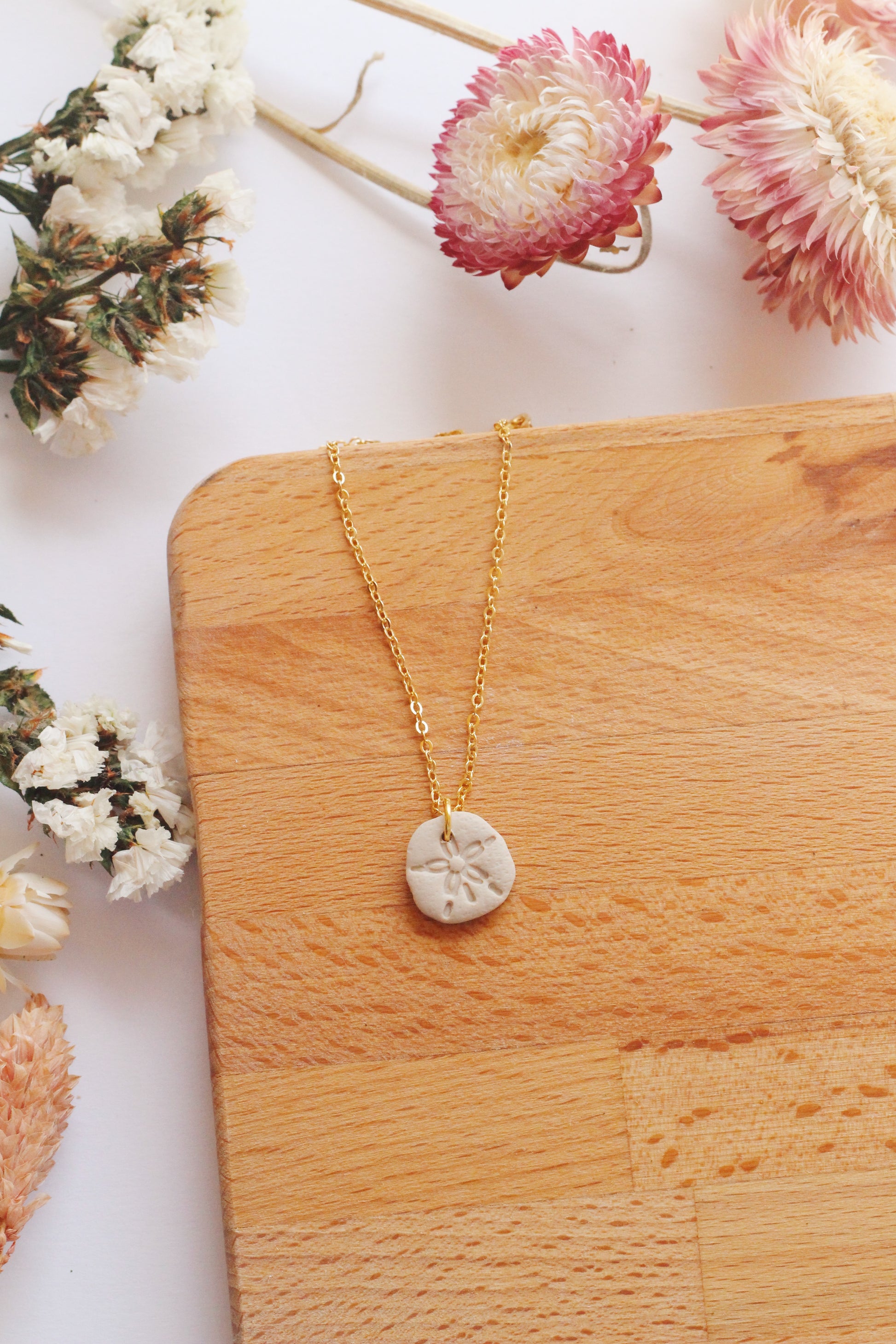 Gold necklace with a sand dollar pendant on a wooden surface surrounded by flowers
