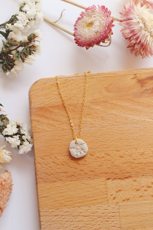 Gold necklace with a sand dollar pendant on a wooden surface surrounded by flowers