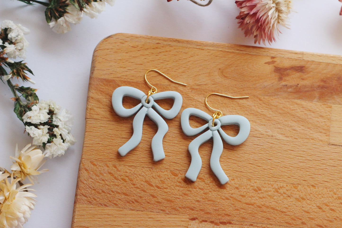Blue bow-shaped earrings on a wooden board with flowers in the background