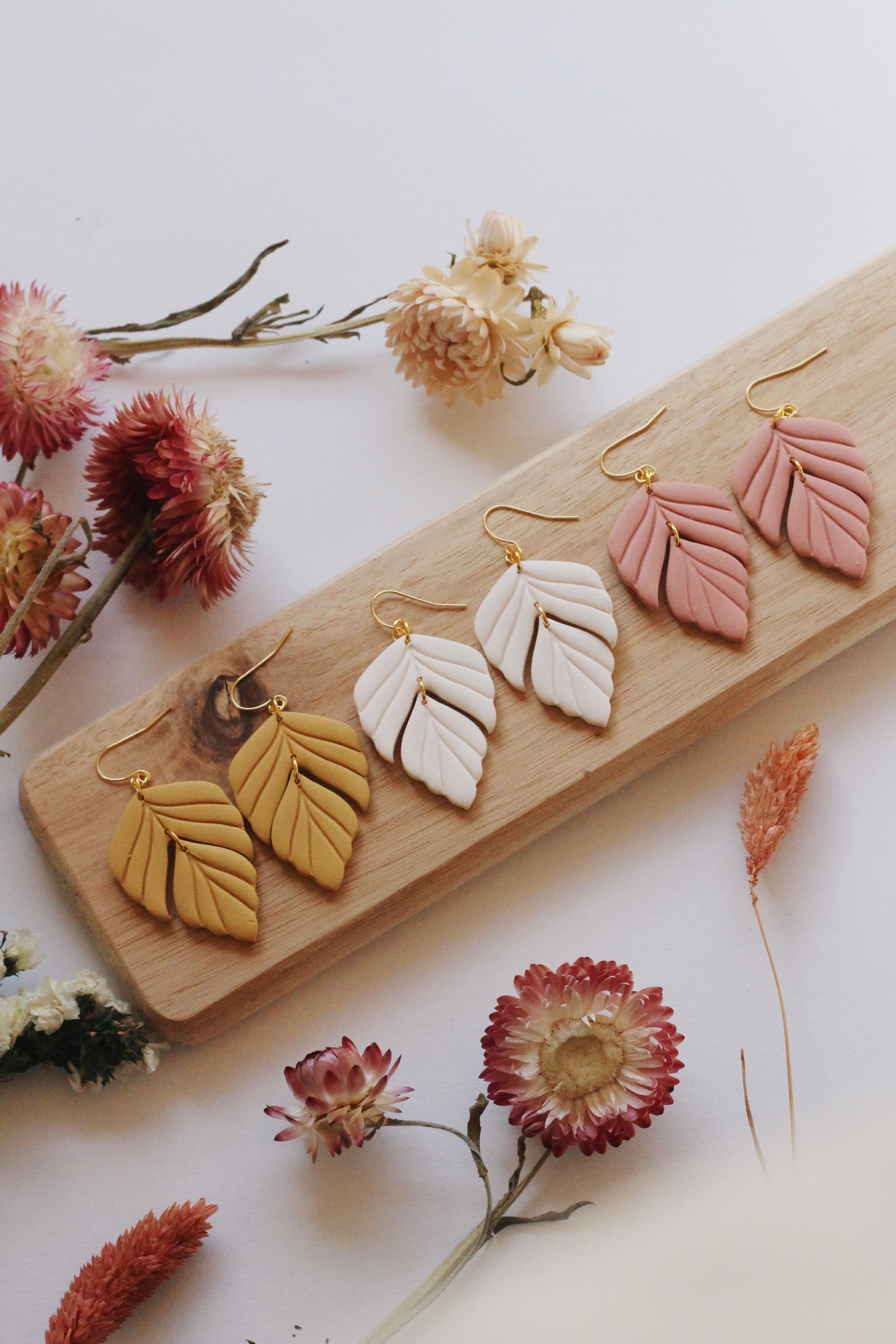 Leaf-shaped earrings on a wooden board with flowers around