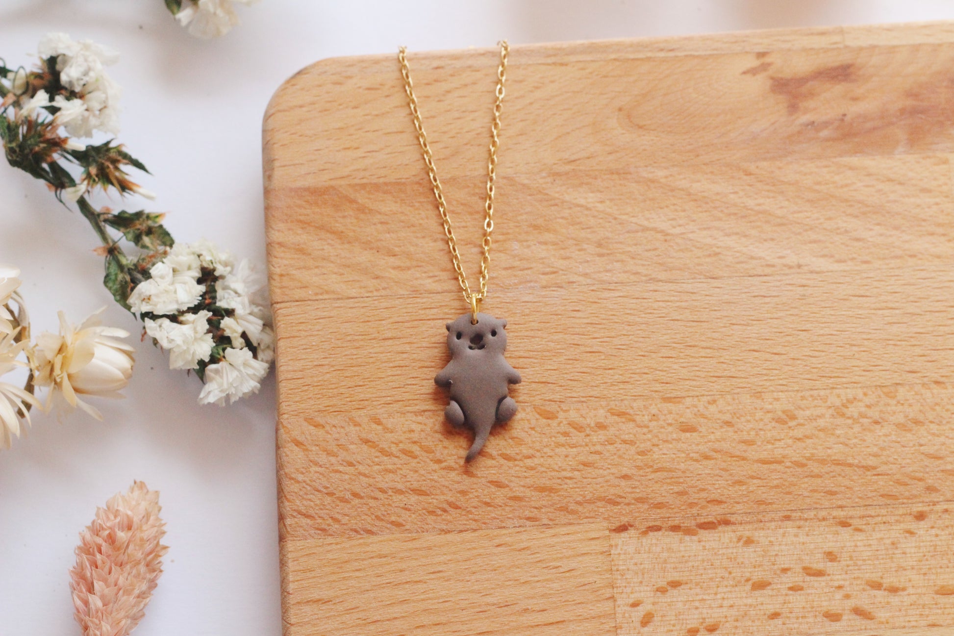 Necklace with an otter pendant on a wooden surface with flowers in the background