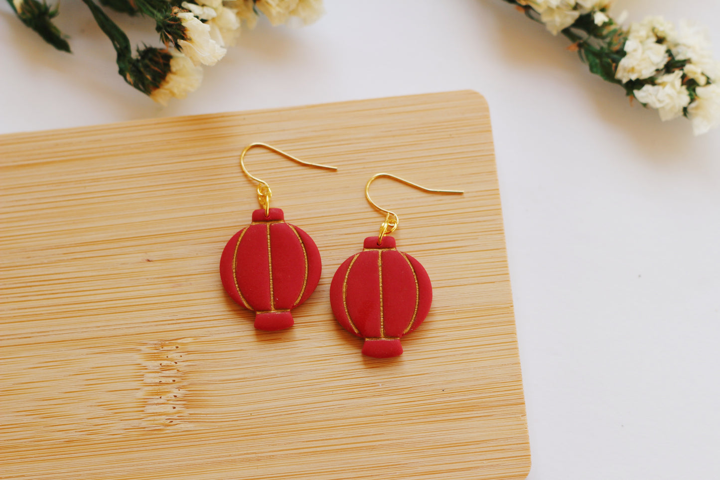 Red lantern-shaped earrings on a wooden board with flowers in the background